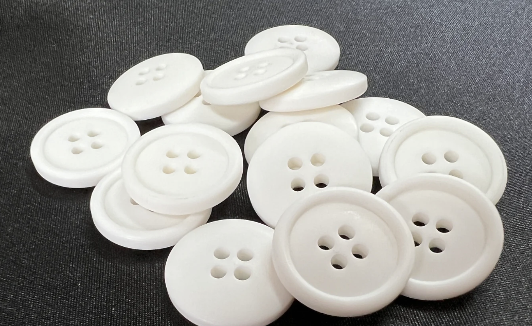 White polyester resin buttons with four holes on a dark fabric background in a pile