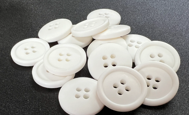 White polyester resin buttons with four holes on a dark fabric background in a pile