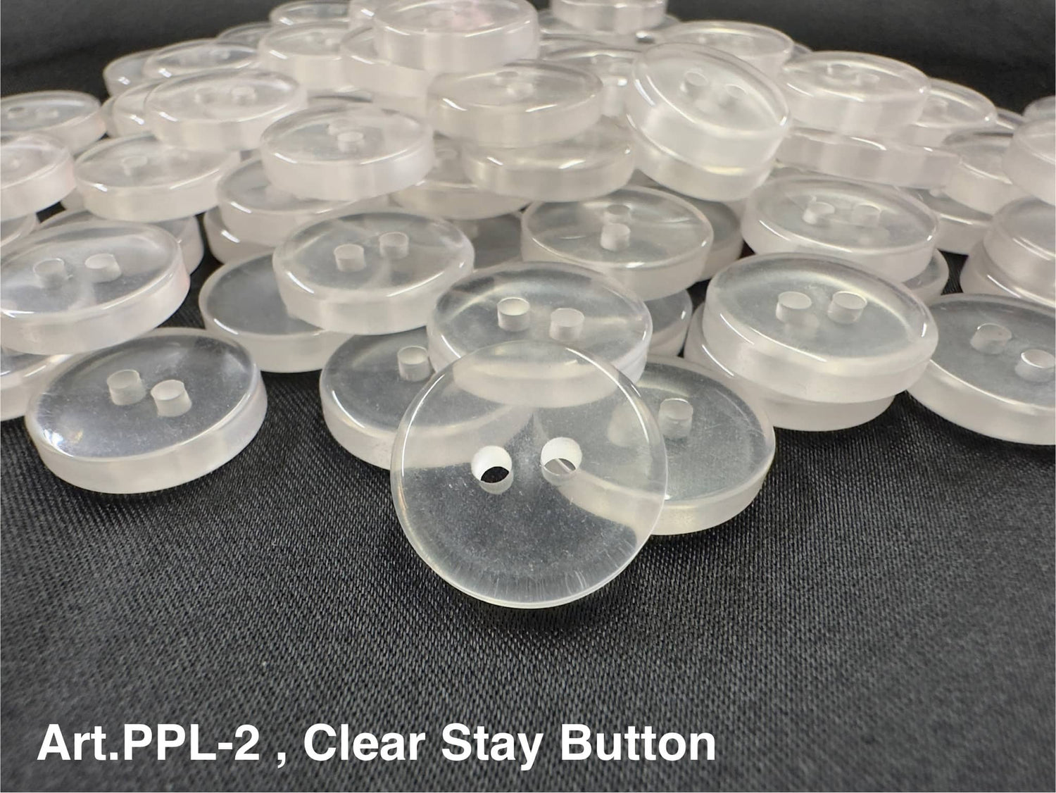 Clear custom sew through buttons with two holes laid out on a dark fabric surface