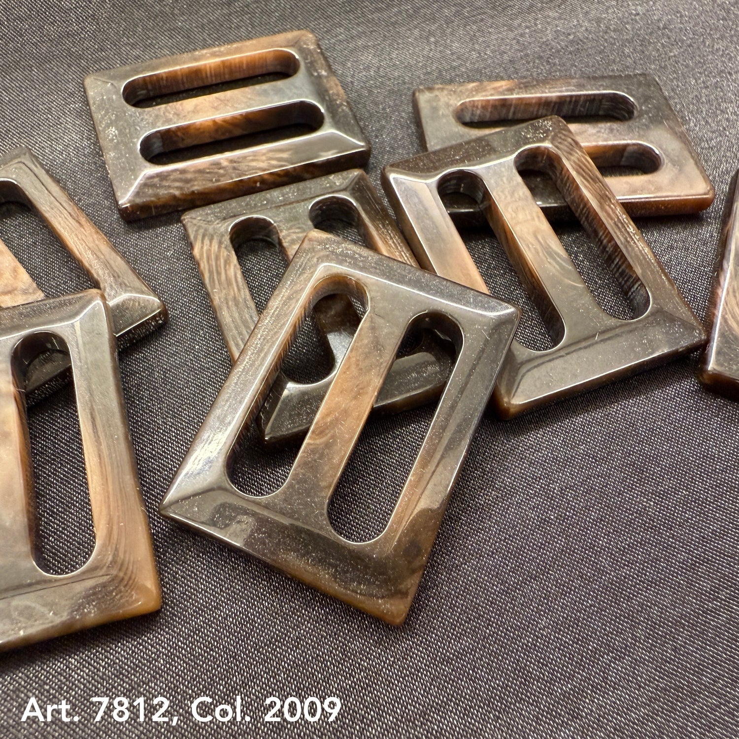 Close-up of fashion buckles for garments in various shades of brown arranged on dark fabric