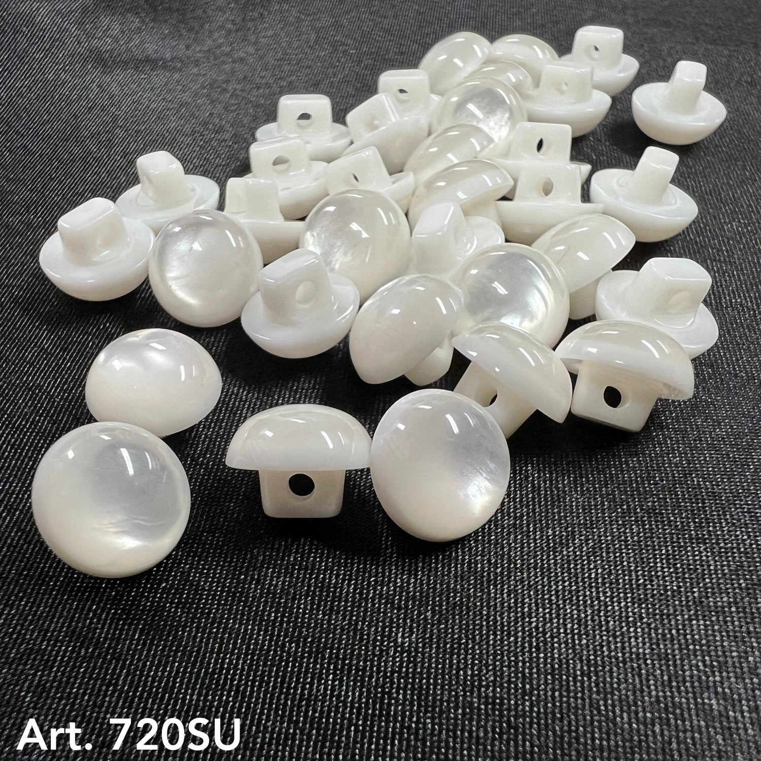 Glossy white traditional shank buttons scattered on dark fabric for clothing and upholstery