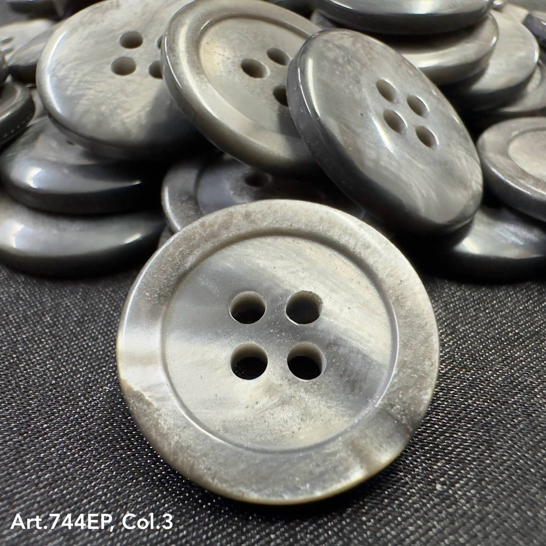 Gray 4-hole plastic buttons by Buttonology Inc stacked on black fabric background