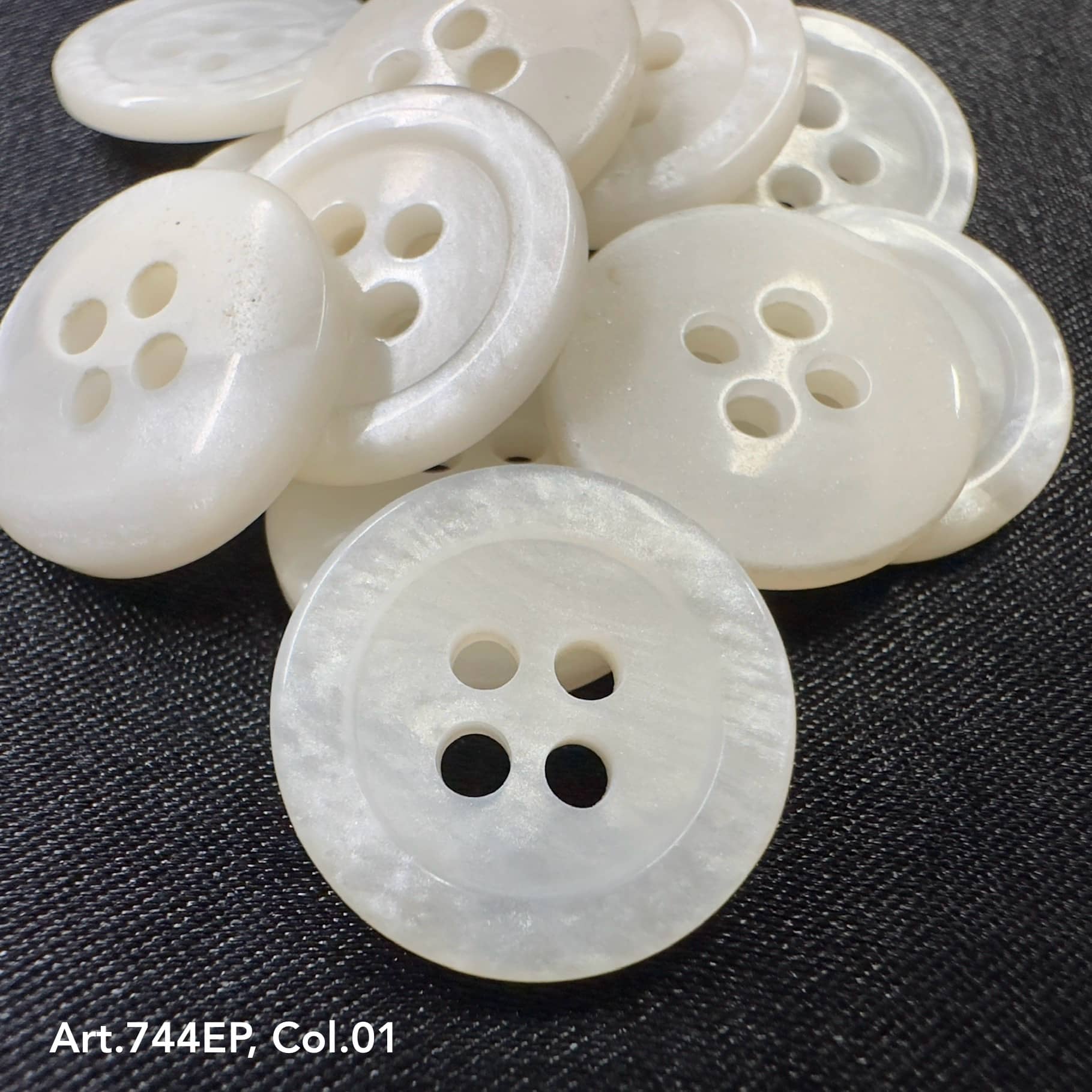 White 4-hole plastic buttons by Buttonology Inc. arranged on a dark fabric background