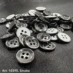 4-hole white buttons and smoke gray buttons from Buttonology Inc spread on dark fabric background
