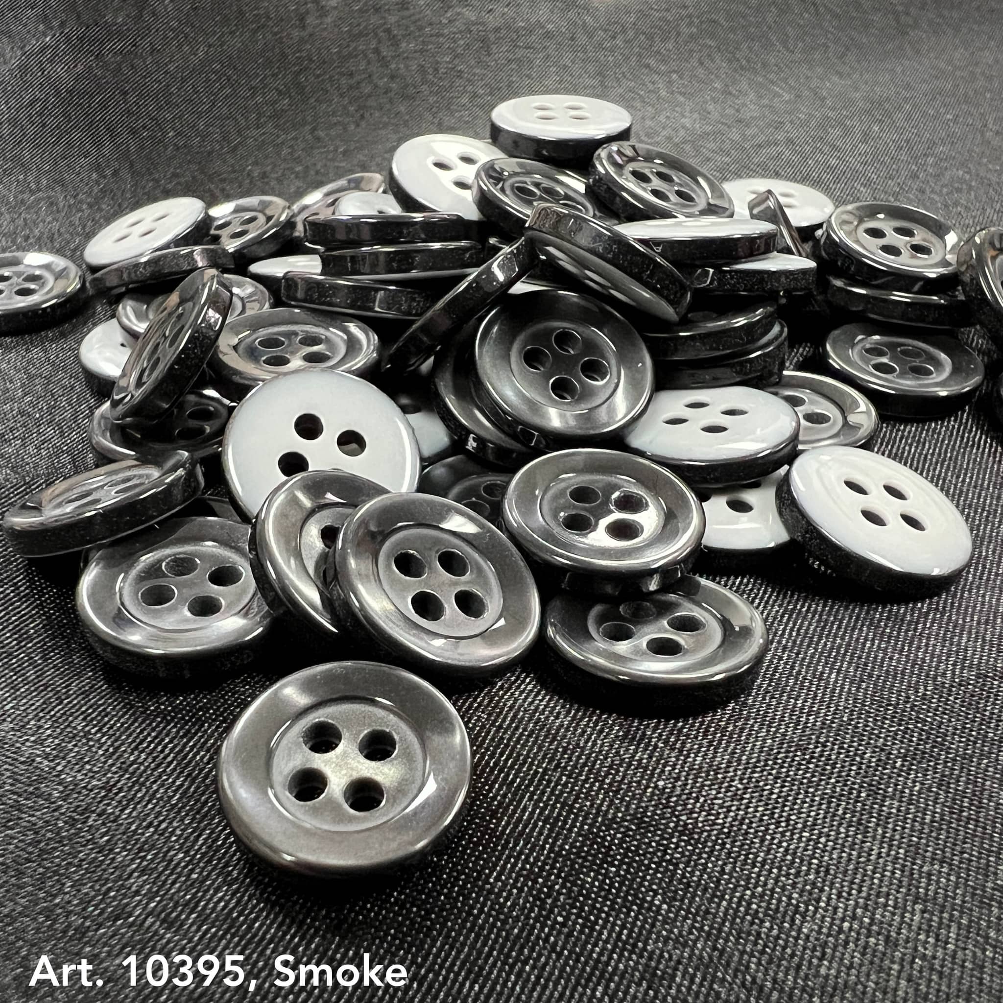 4-hole white buttons and smoke gray buttons from Buttonology Inc spread on dark fabric background