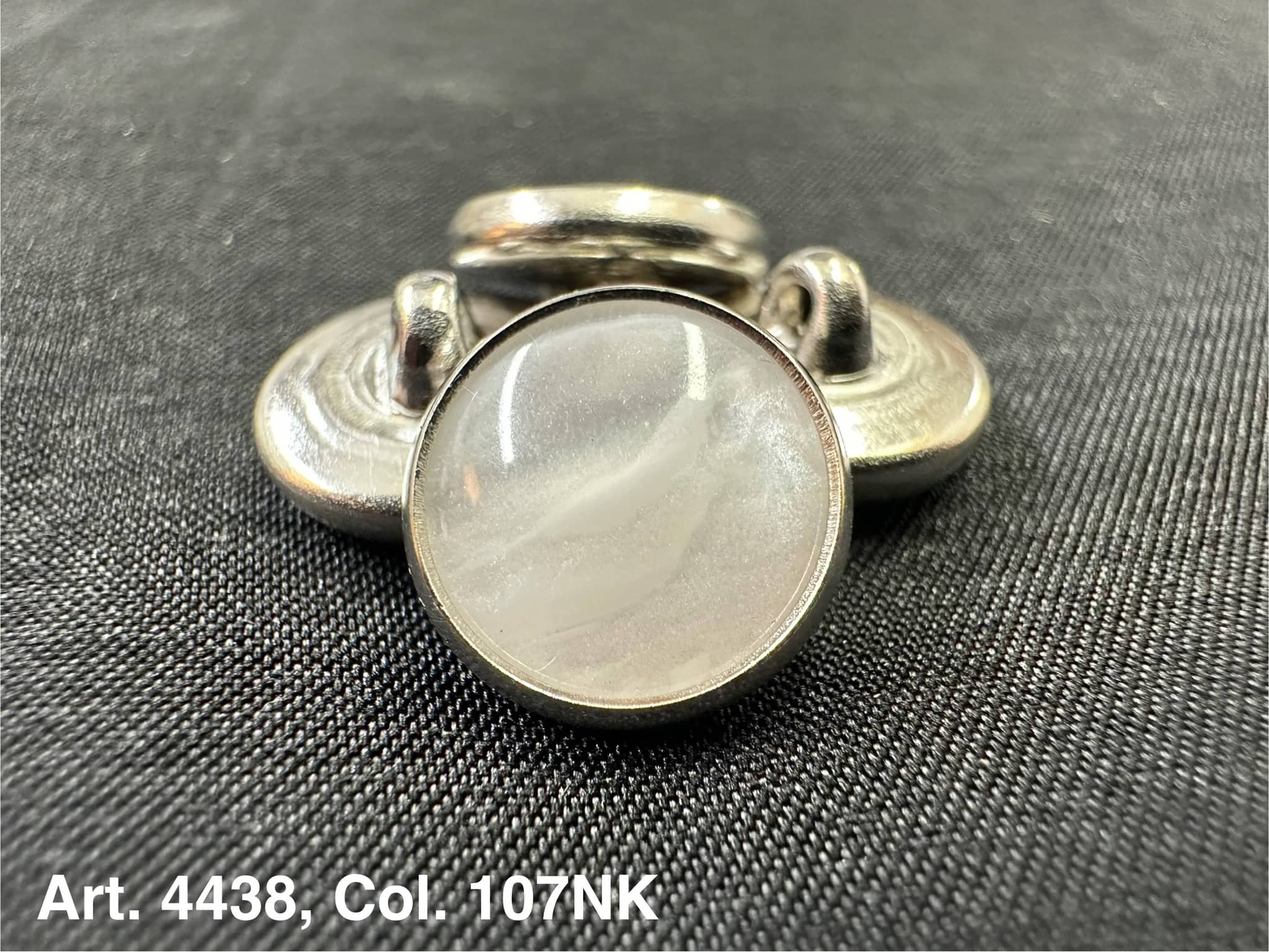 Buttonology Inc polyester garment shank with pearlescent white cabochon and silver metal rim on black fabric