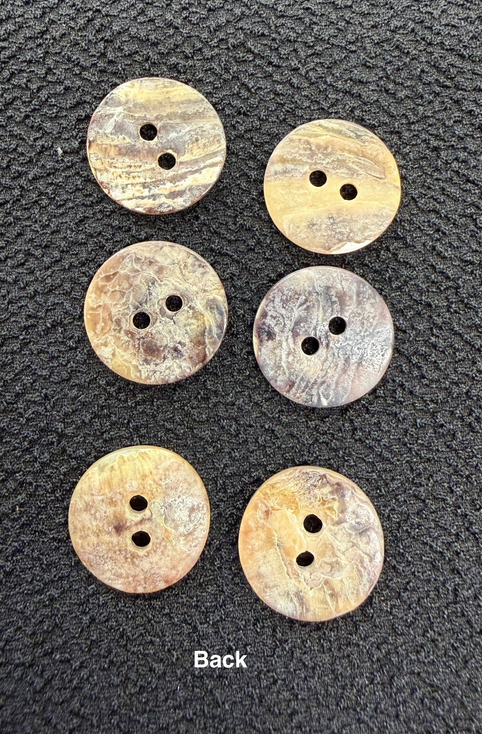Six round buttons with two holes on a textured black surface
