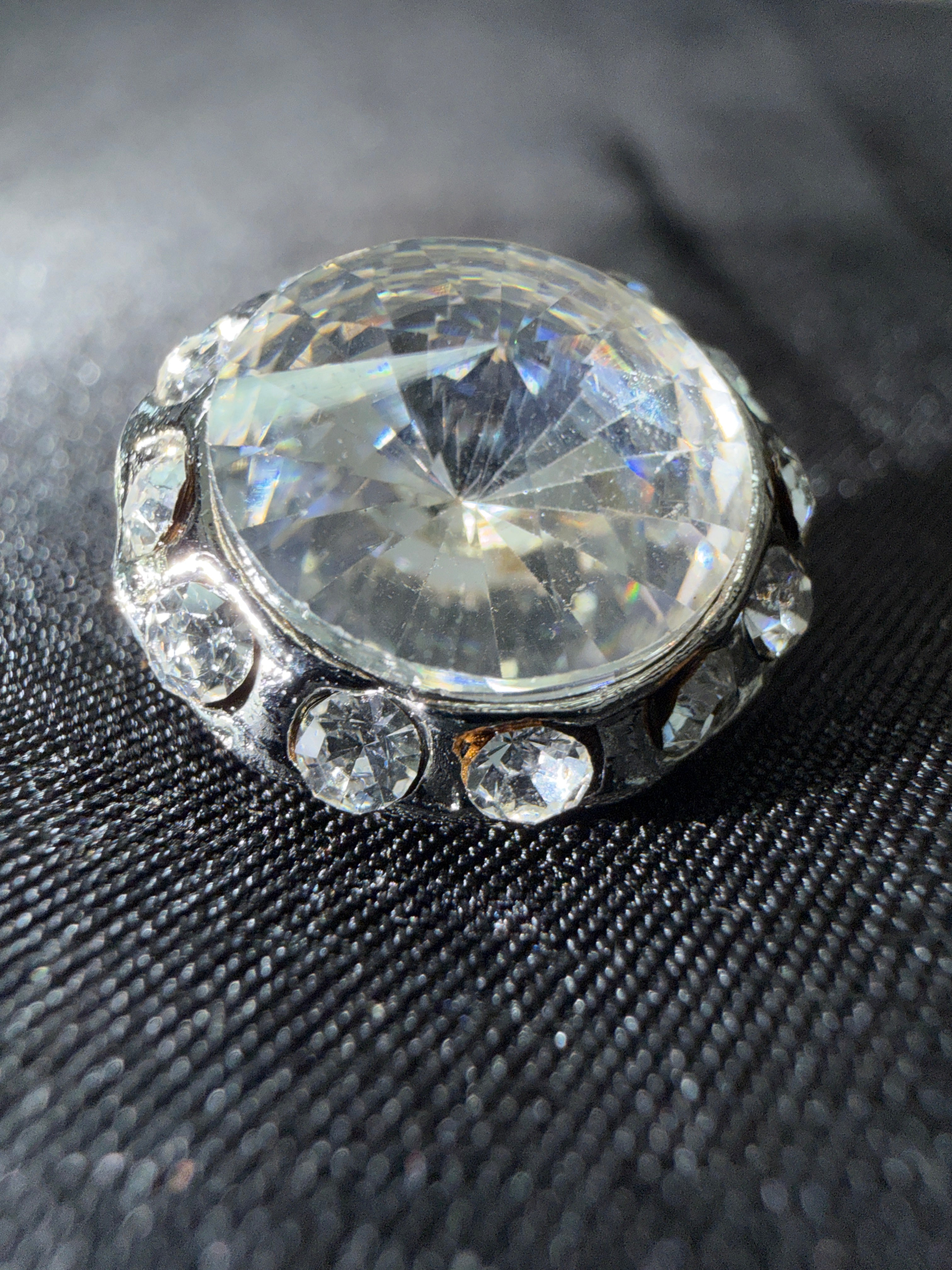 Close-up of a ring with a large central diamond and smaller diamonds on a textured black background