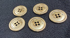 Five brass buttons with four-hole design on a textured dark surface