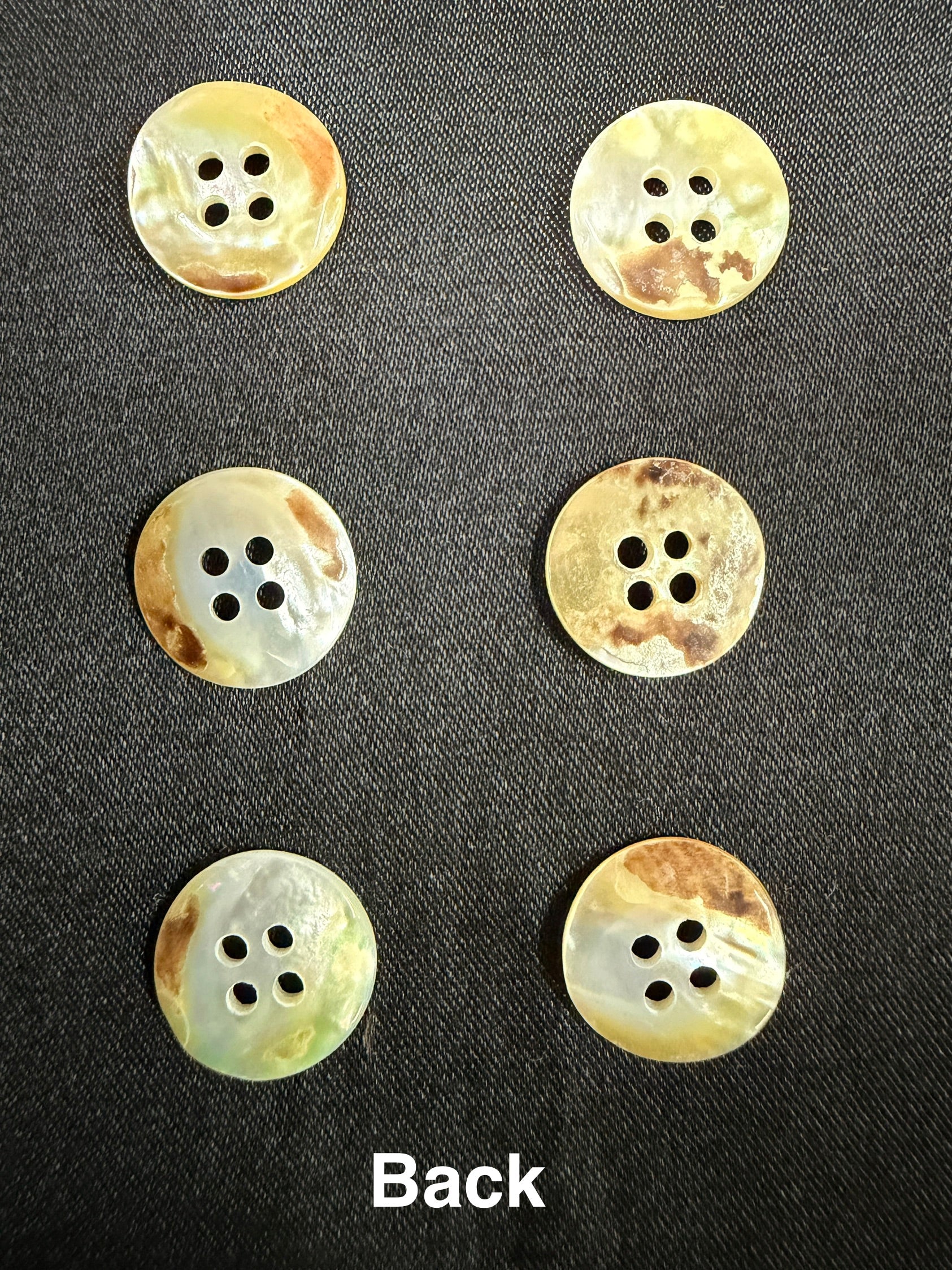 Set of six beige buttons with brown spots on a black background