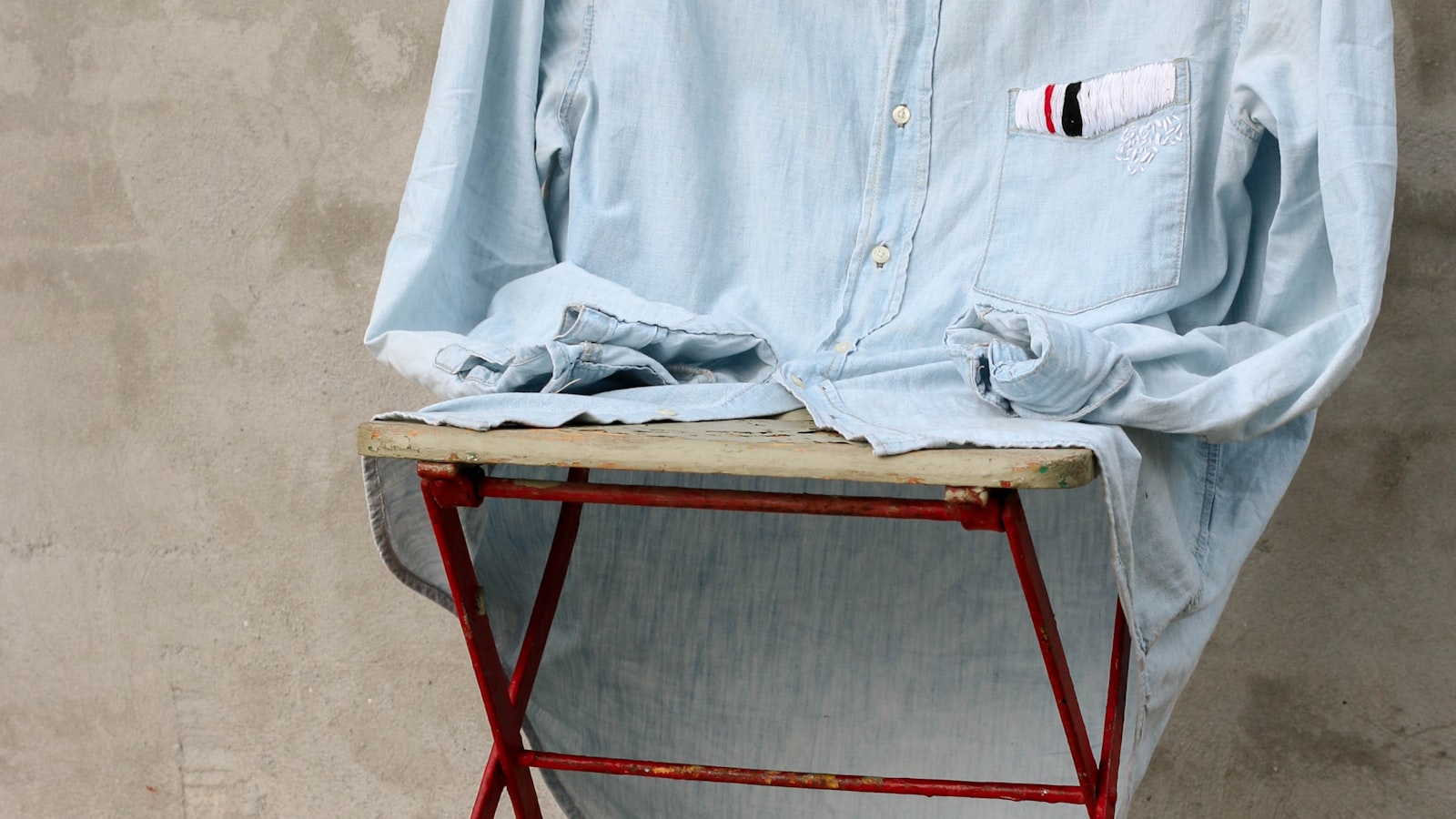 Light blue denim shirt on a red metal stool against a beige wall