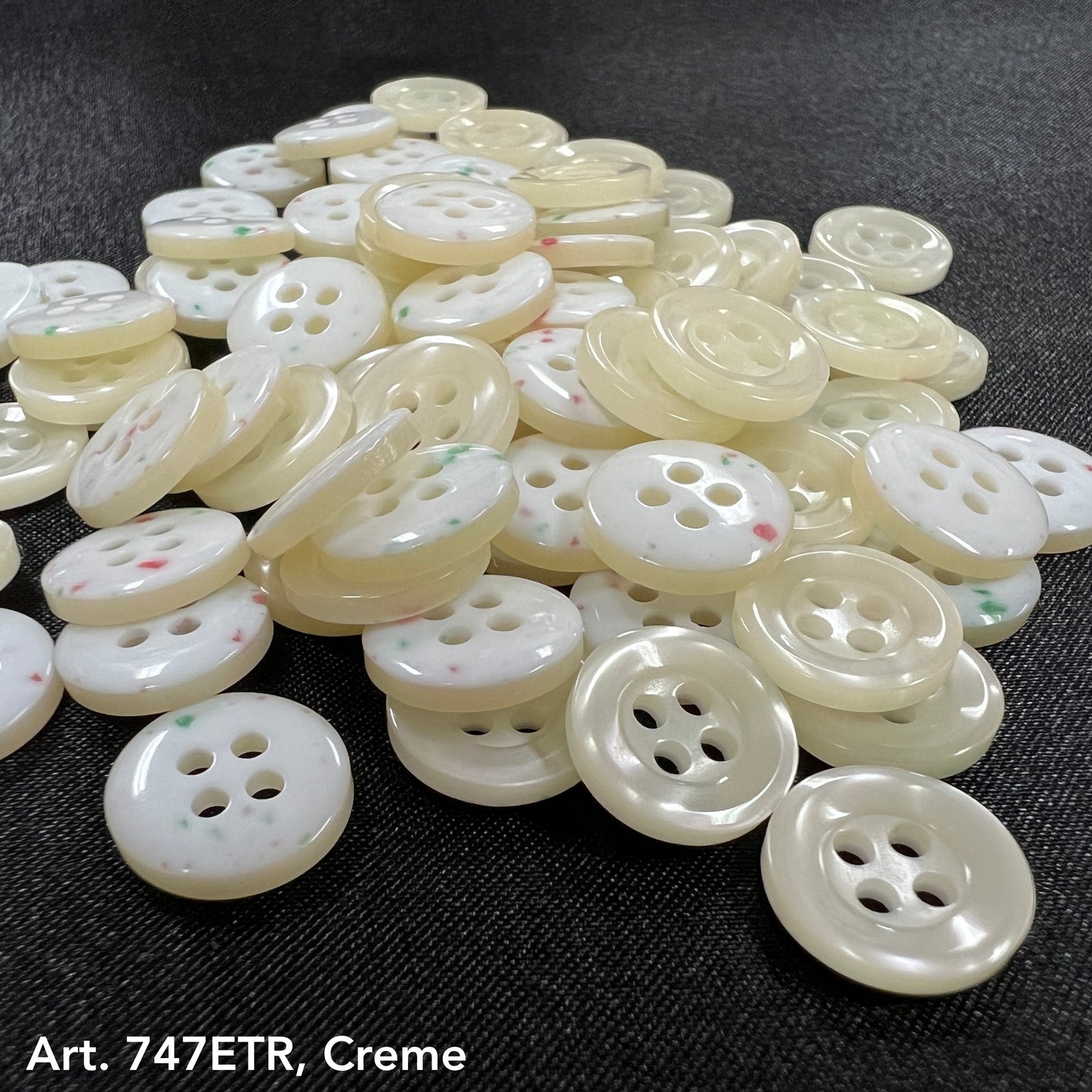 Pile of smoke four-hole buttons in cream color from Buttonology Inc on black fabric background