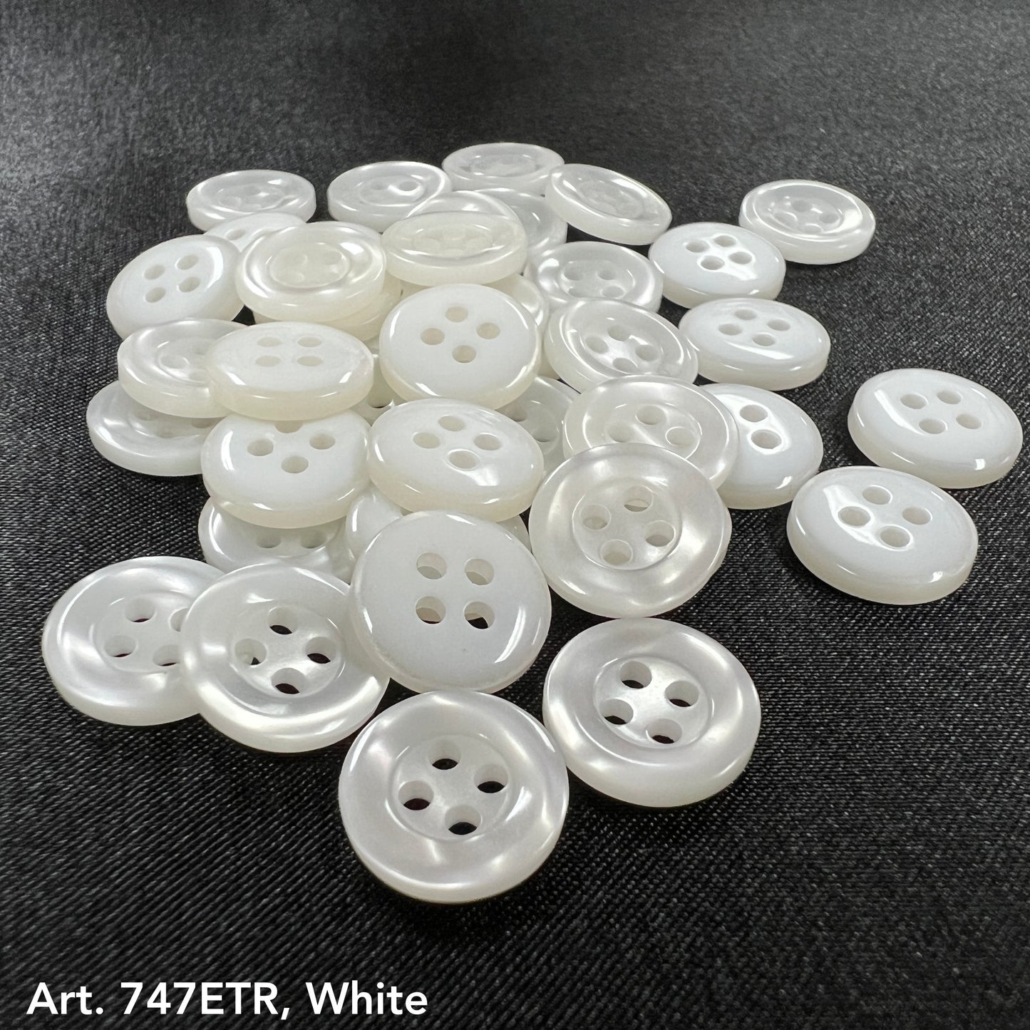 Buttonology Inc smoke four-hole buttons in white arranged on black fabric surface
