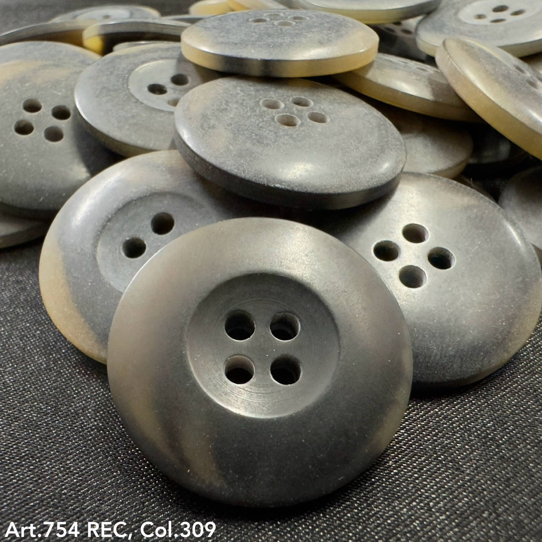 Gray buttons with four holes stacked on black fabric showcasing custom button designs by Buttonology Inc