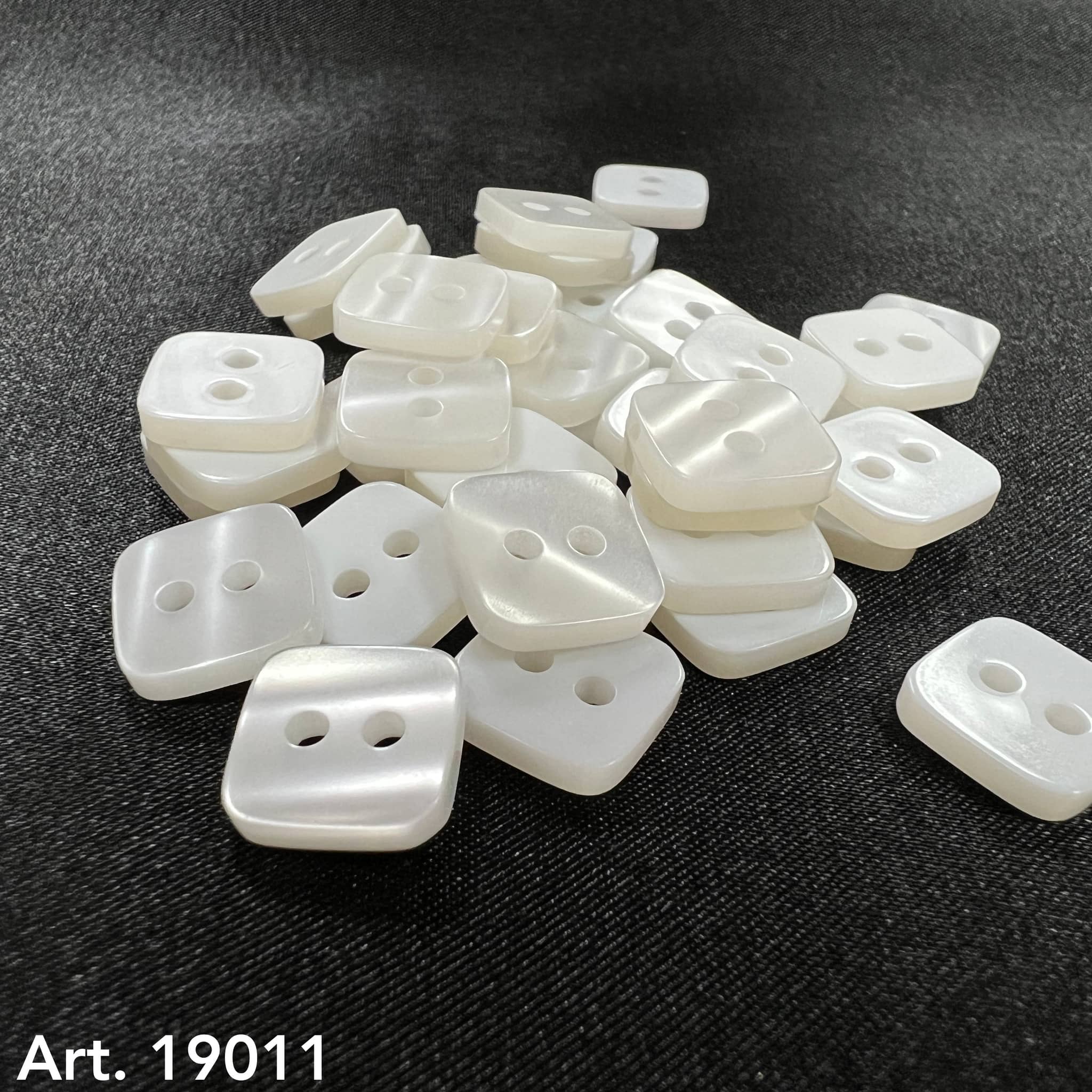Square pearl buttons by Buttonology Inc in a pile on black fabric background