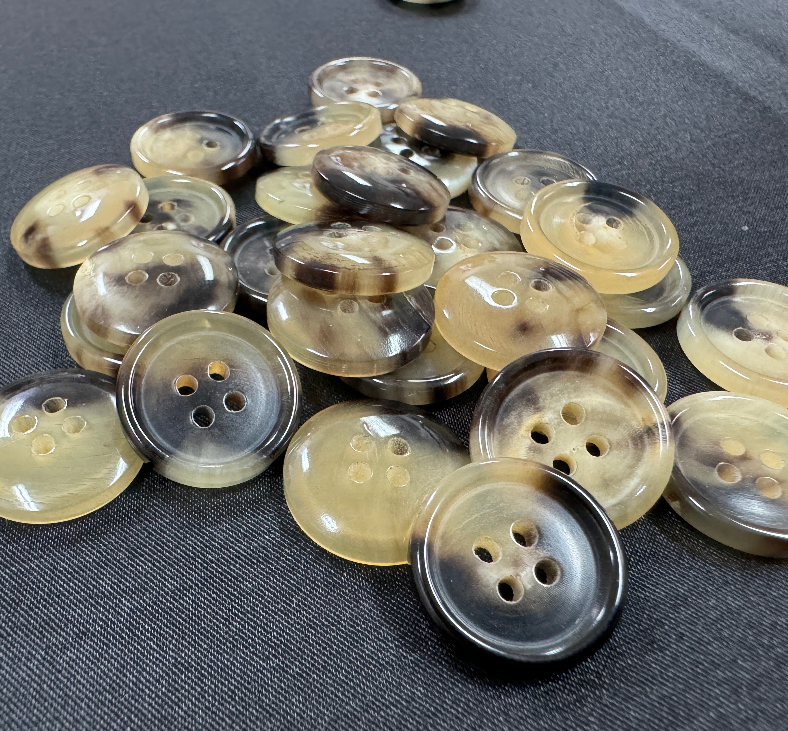 Pile of sustainable real horn buttons by Buttonology Inc in natural brown and beige tones with four holes