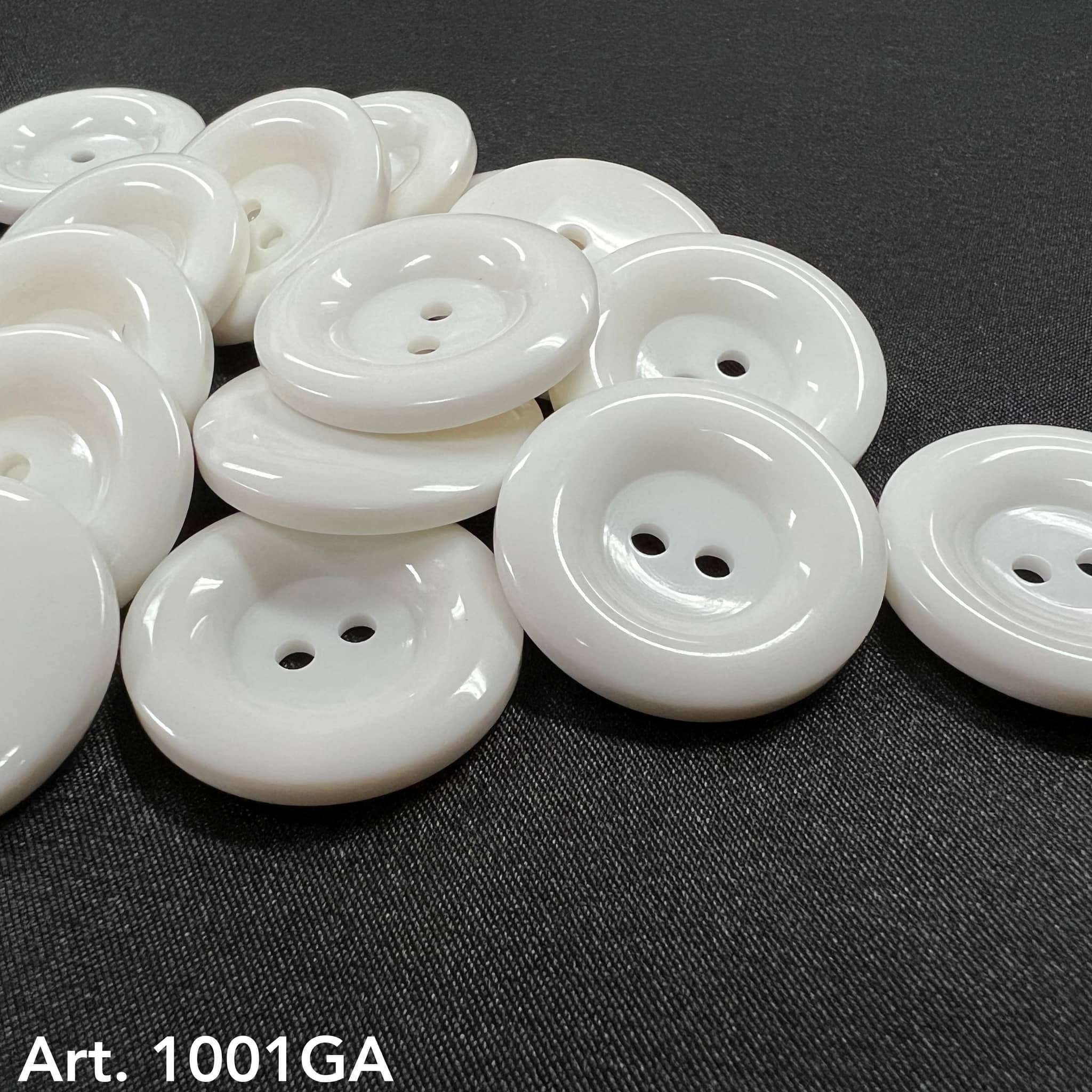 White glossy two hole round buttons on dark fabric by Buttonology Inc white garment buttons for sewing projects