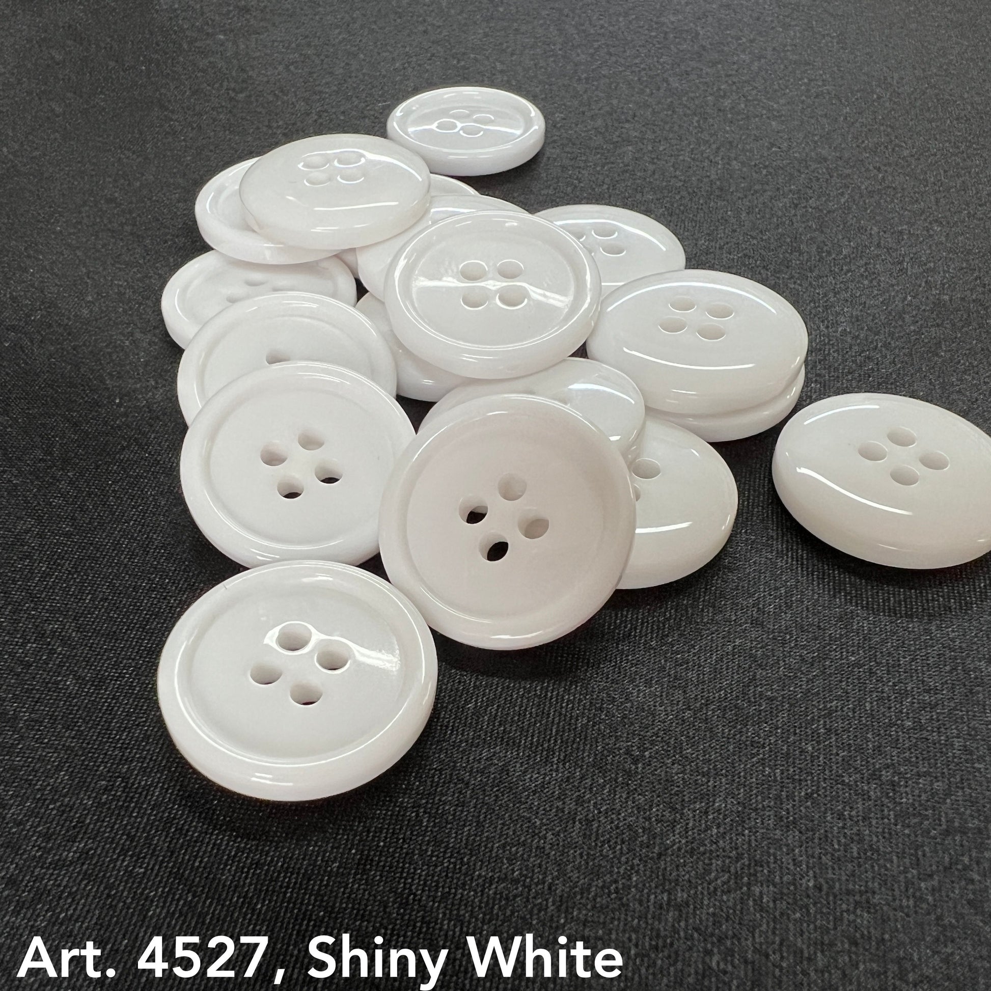 Basic white 4-hole buttons by Buttonology Inc with shiny finish on a dark fabric background