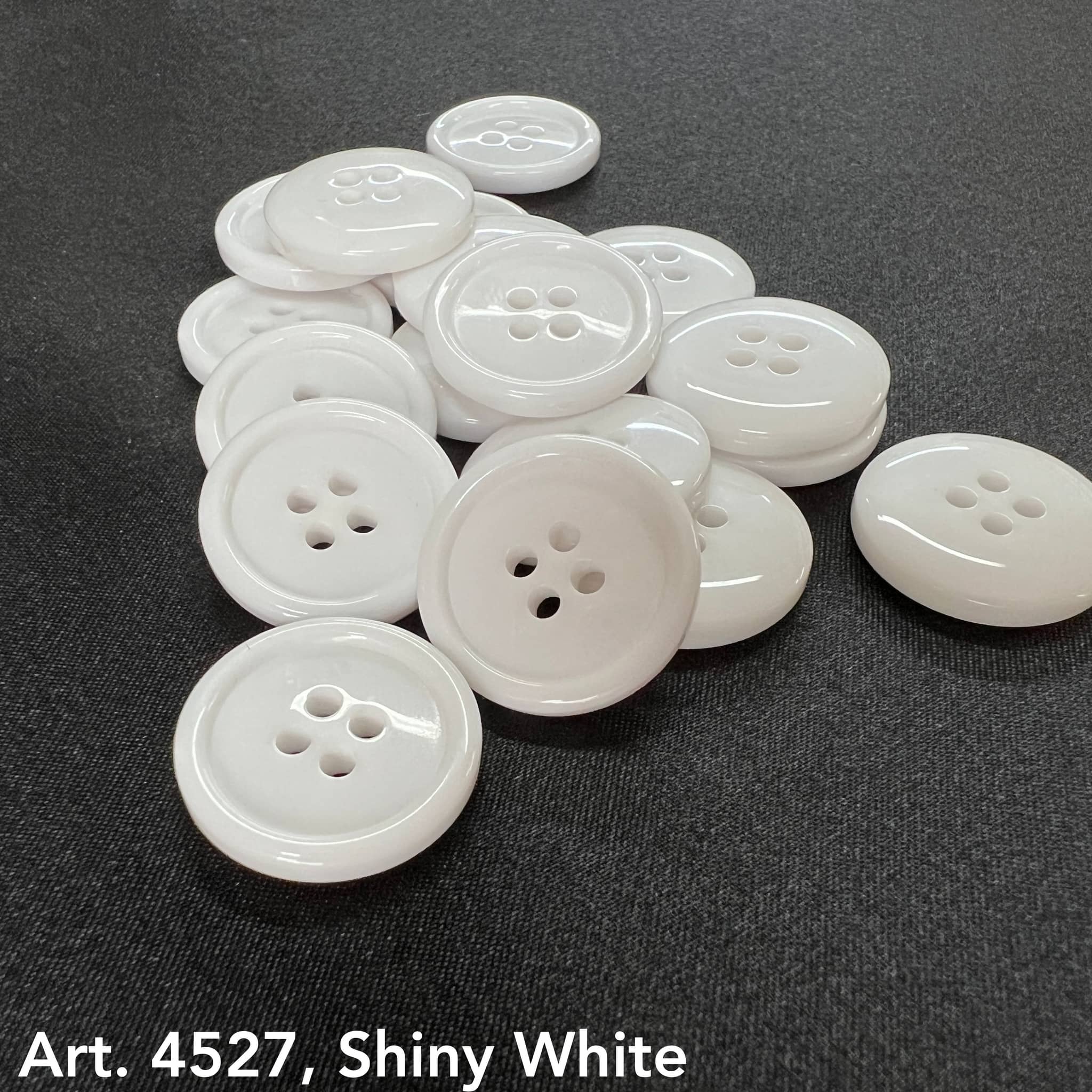 Basic white 4-hole buttons by Buttonology Inc with shiny finish on a dark fabric background