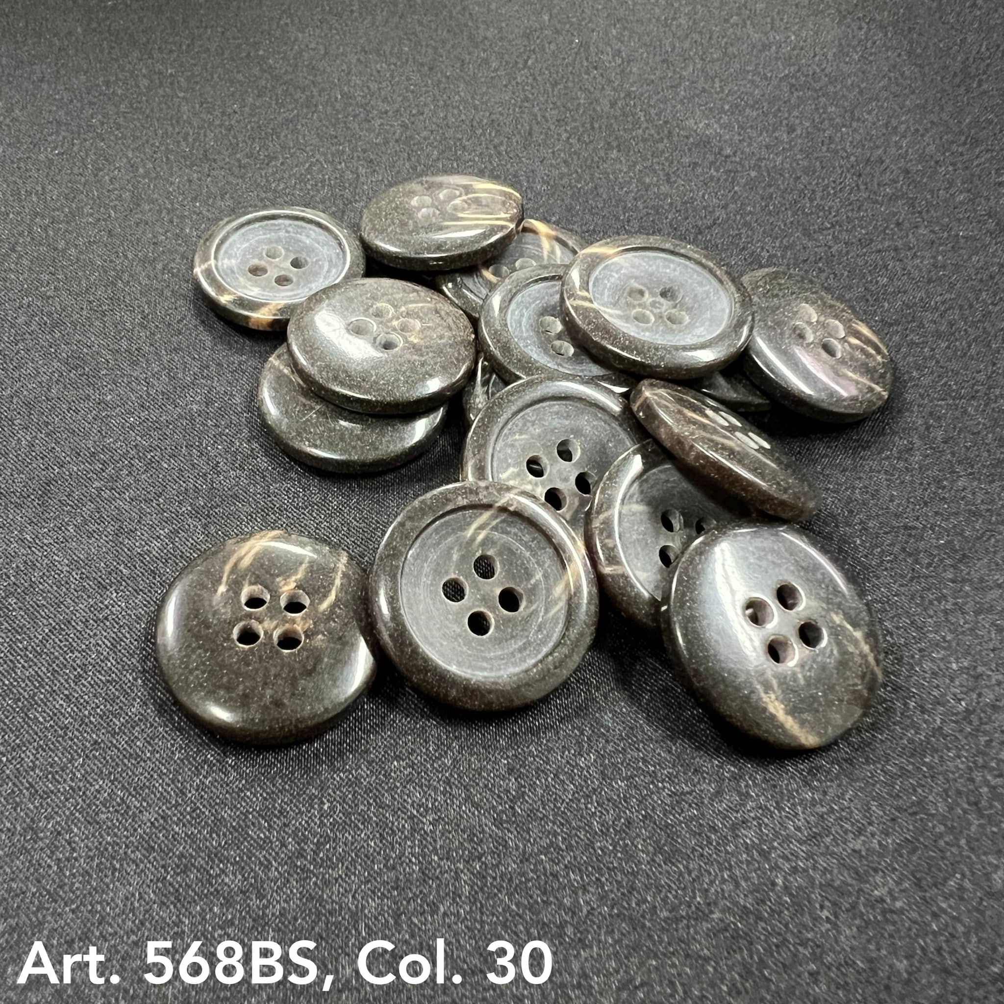 Collection of black 4-hole garment buttons from Buttonology Inc on a black fabric background