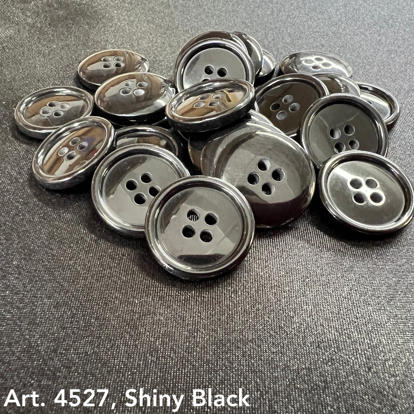 Black four hole buttons for sewing arranged on a dark surface, showcasing their shiny finish