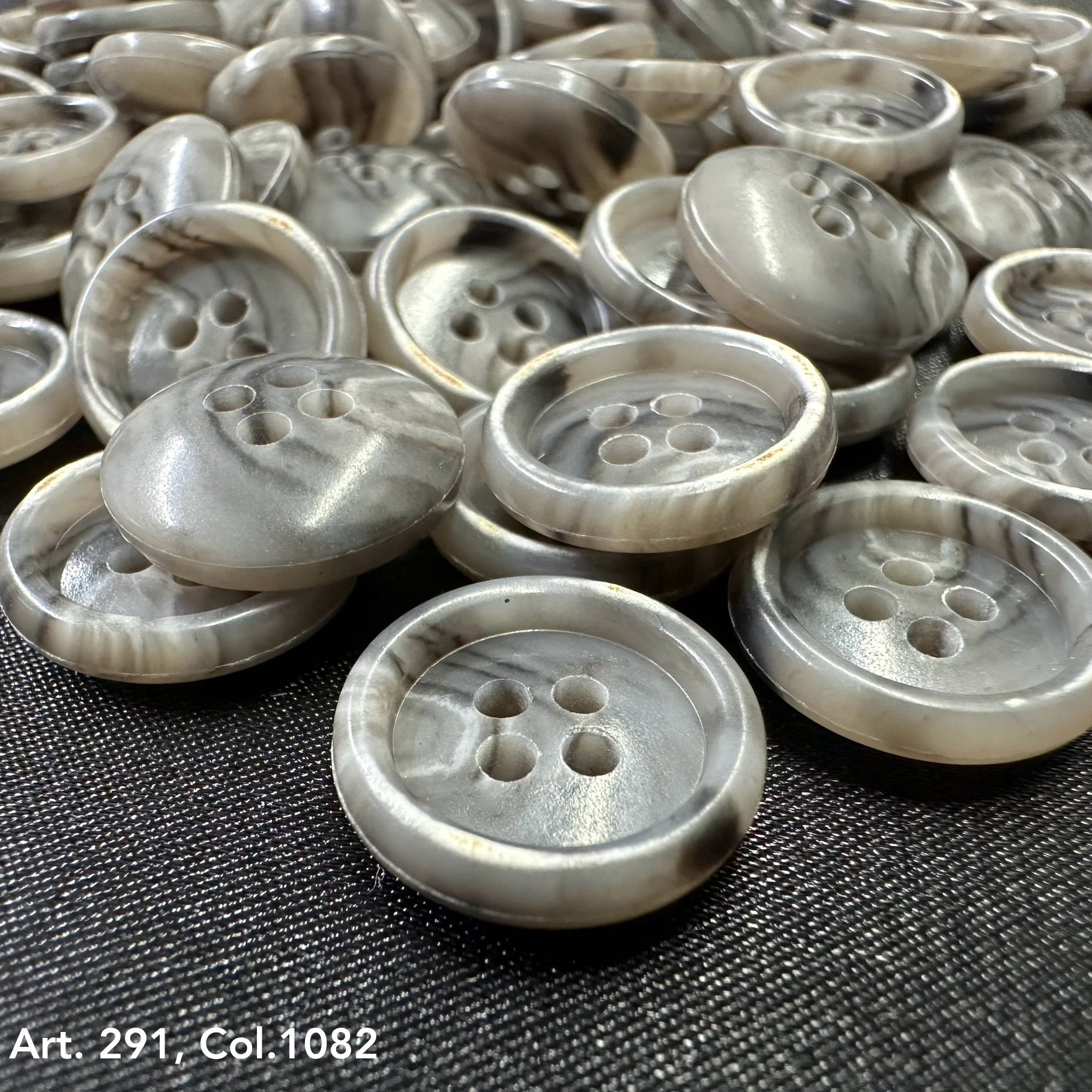 Assorted grey coat buttons for sewing displayed in a pile, featuring a four-hole design