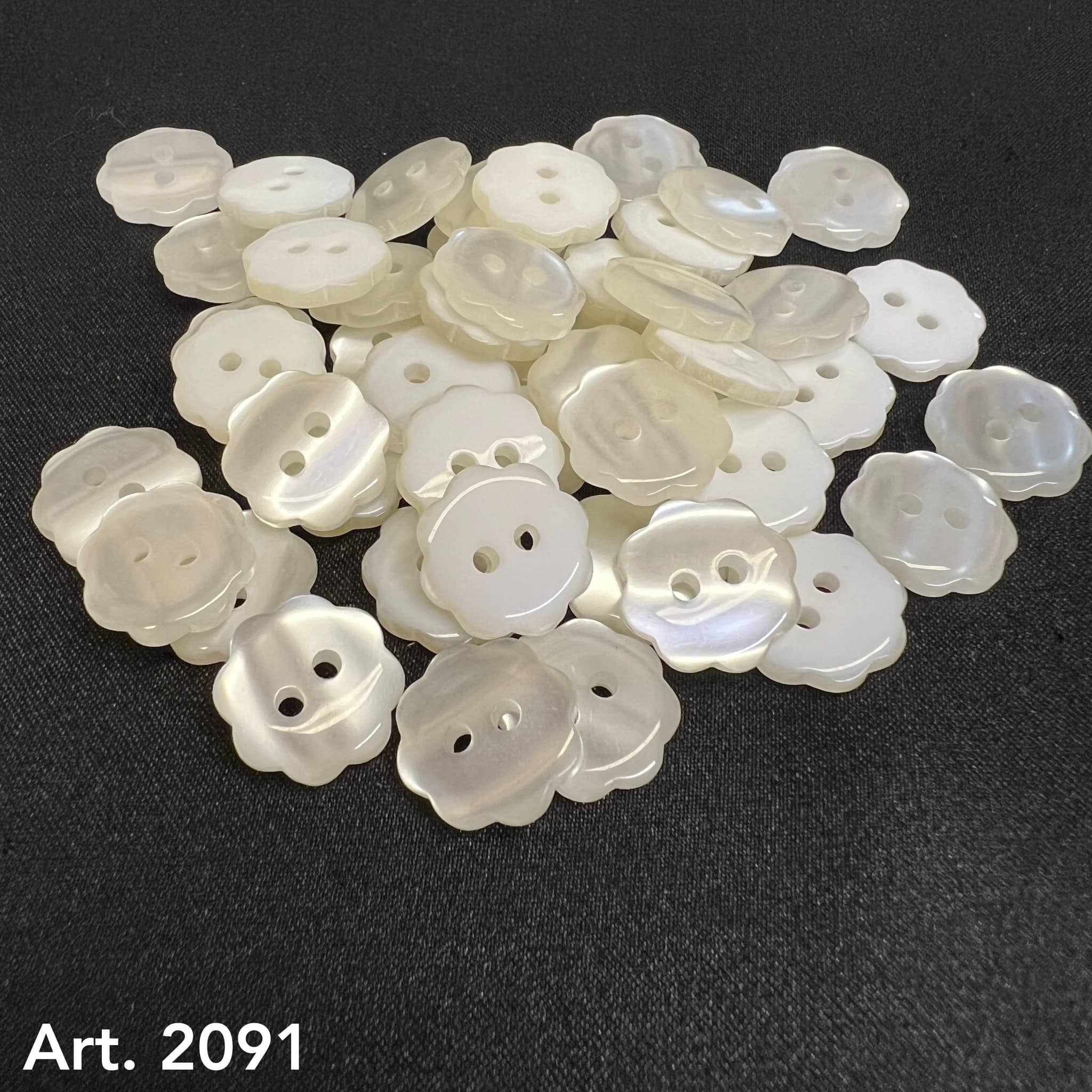 Buttonology Inc custom flower buttons in pearly white with two holes laid on black fabric background