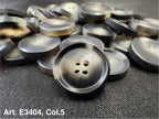 Buttonology Inc grey round plastic four hole sewing buttons stacked on fabric showing matte and glossy finishes