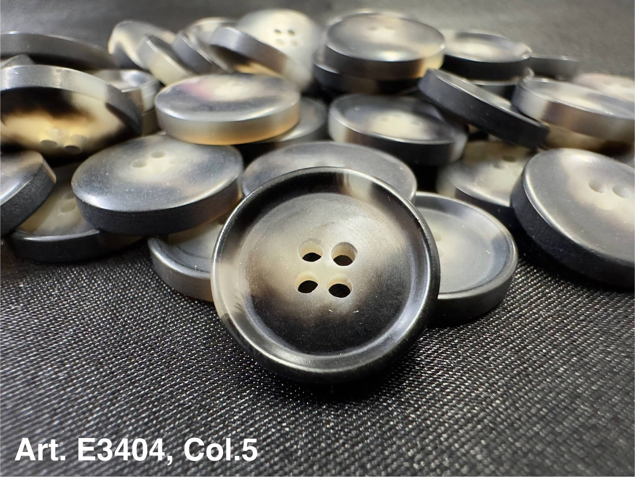 Buttonology Inc grey round plastic four hole sewing buttons stacked on fabric showing matte and glossy finishes