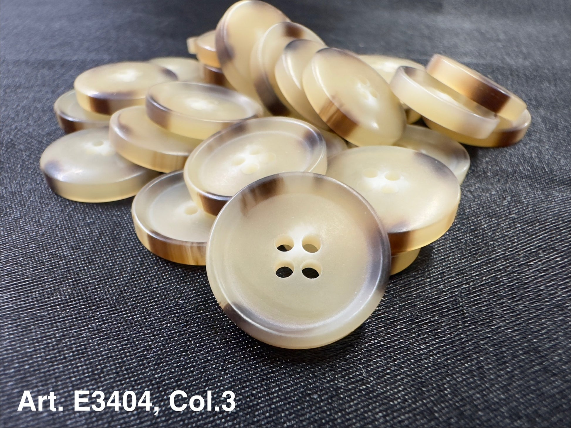 Buttonology Inc beige round buttons with brown rim stacked on dark fabric four hole sewing buttons