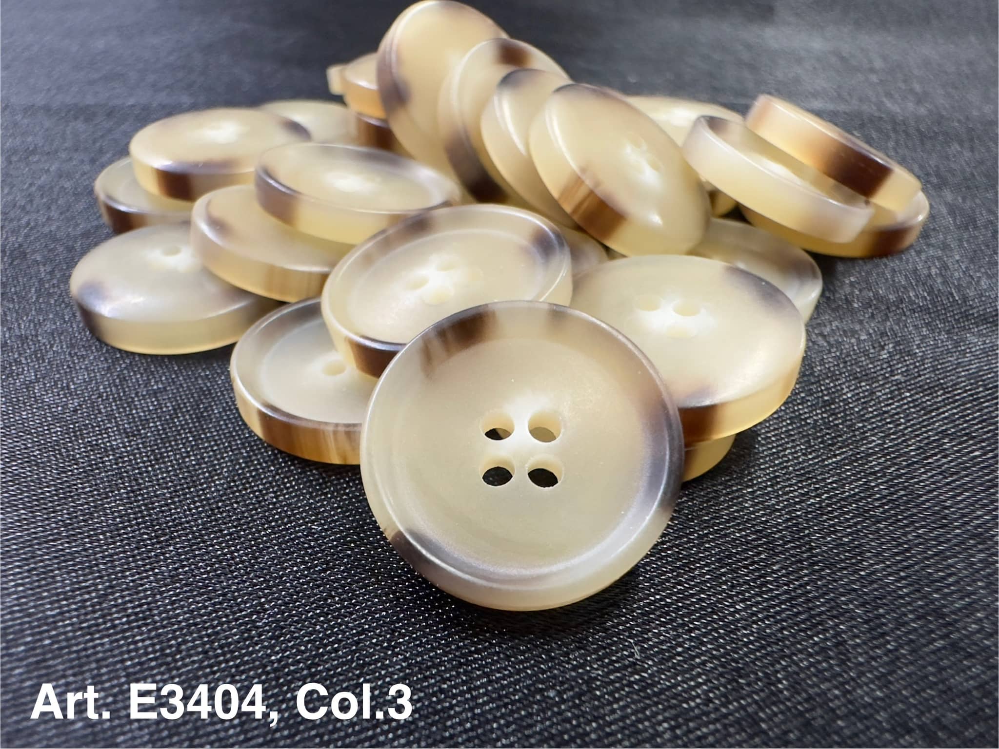 Buttonology Inc beige round buttons with brown rim stacked on dark fabric four hole sewing buttons