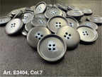 Buttonology Inc matte black plastic four hole sewing buttons piled on black fabric for garments