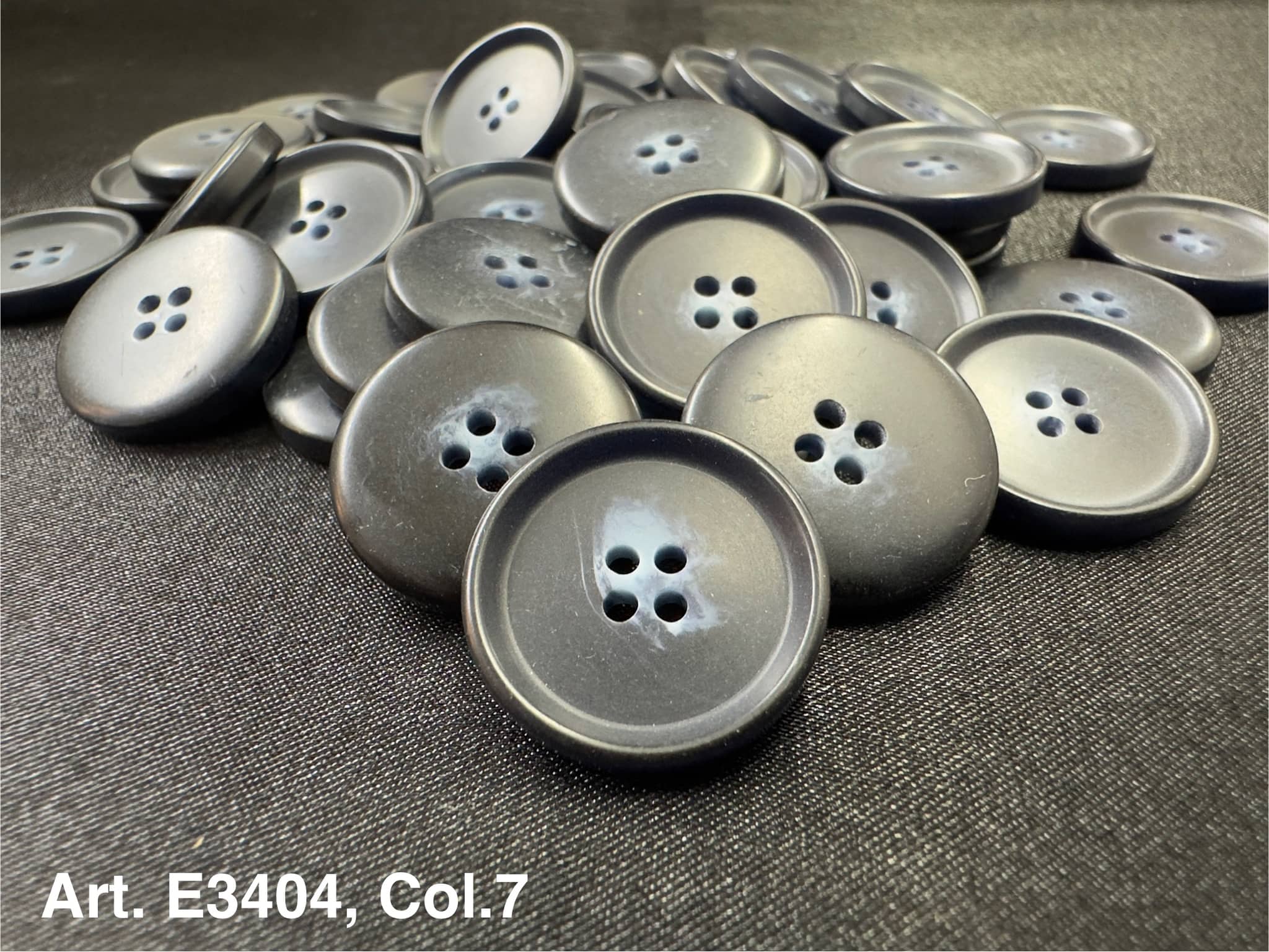 Buttonology Inc matte black plastic four hole sewing buttons piled on black fabric for garments