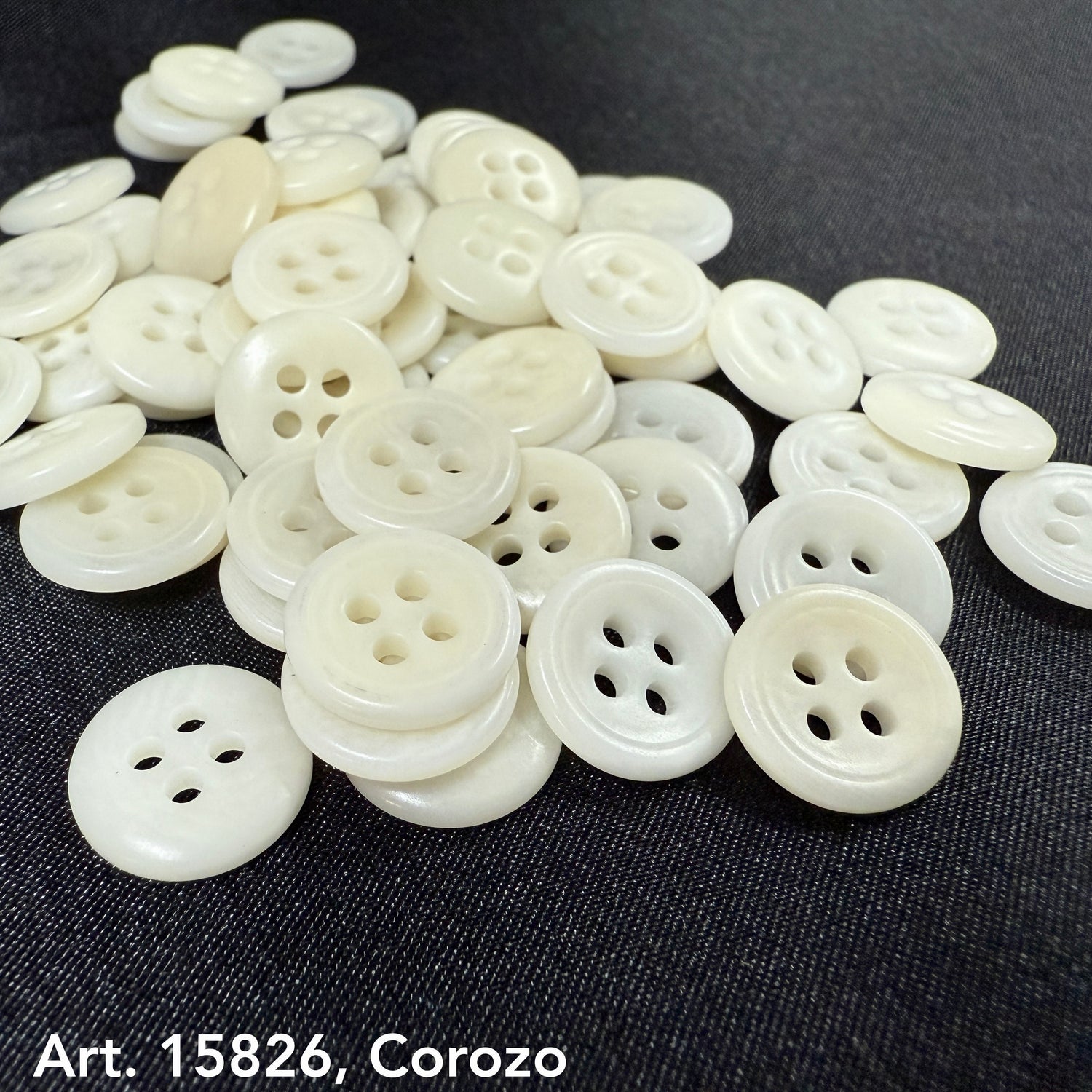 Pile of white Corozo buttons from Buttonology Inc, an eco-friendly button supplier on black fabric background