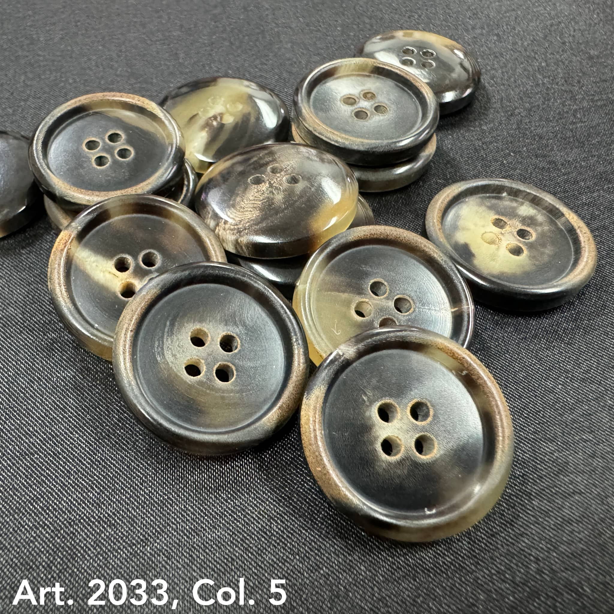 Eco-friendly horn buttons by Buttonology Inc with four holes in natural earthy tones on black fabric