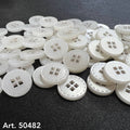 White four-hole clothing buttons from Buttonology Inc. scattered on a black fabric background