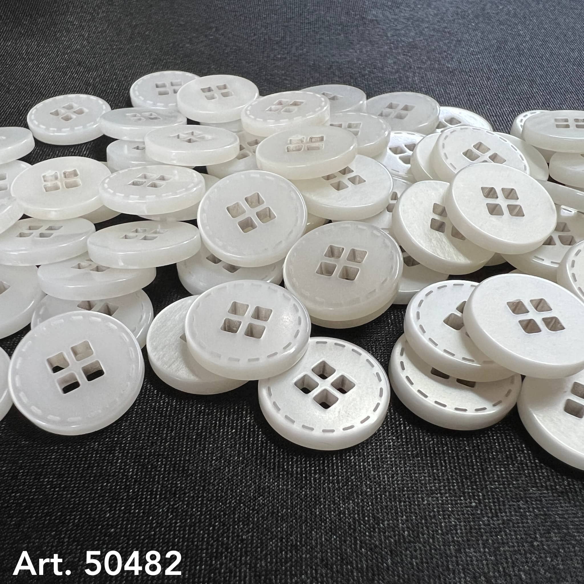 White four-hole clothing buttons from Buttonology Inc. scattered on a black fabric background