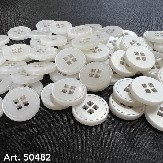 White four-hole clothing buttons from Buttonology Inc. scattered on a black fabric background