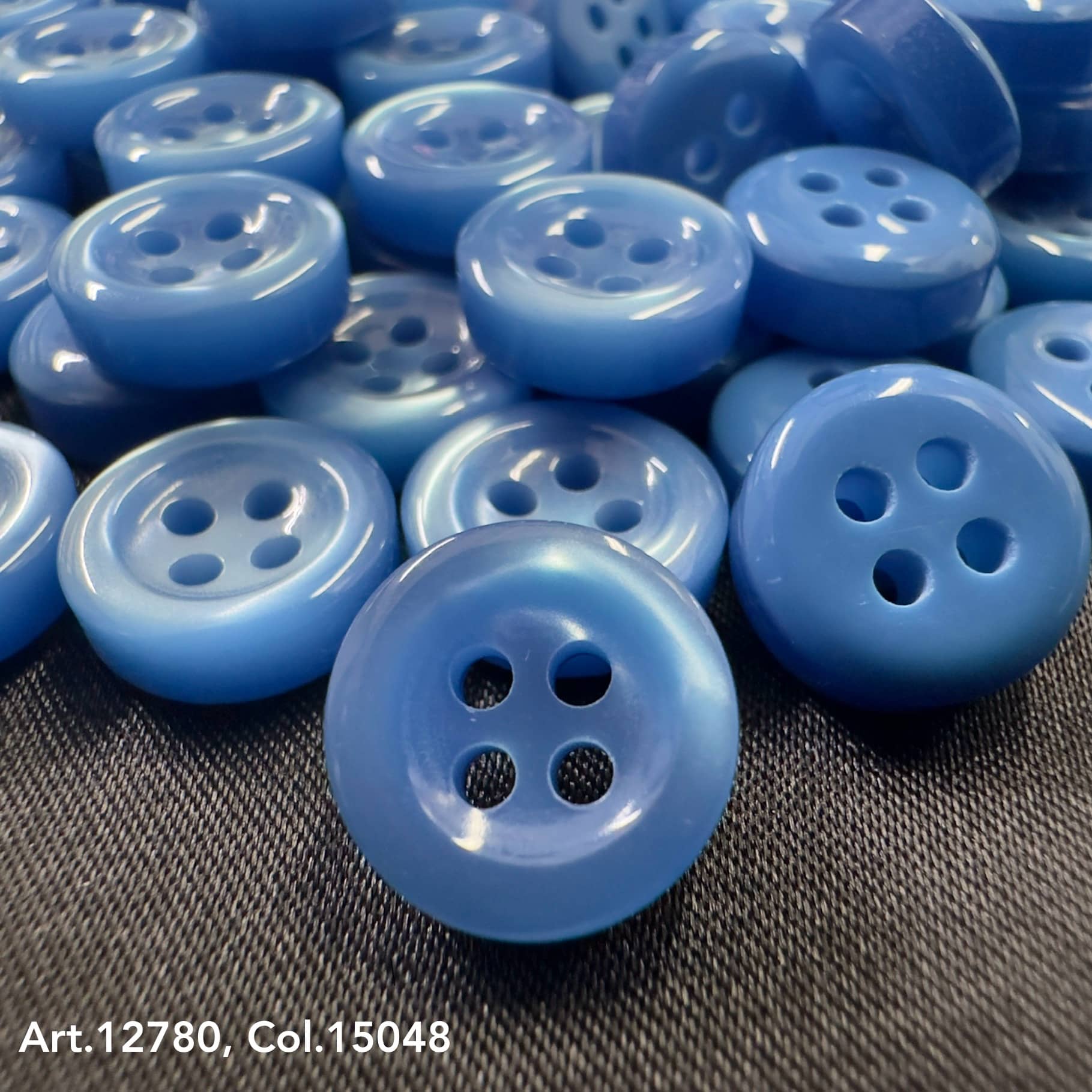 18L four hole plastic buttons in various shades of blue from Buttonology Inc on black fabric background