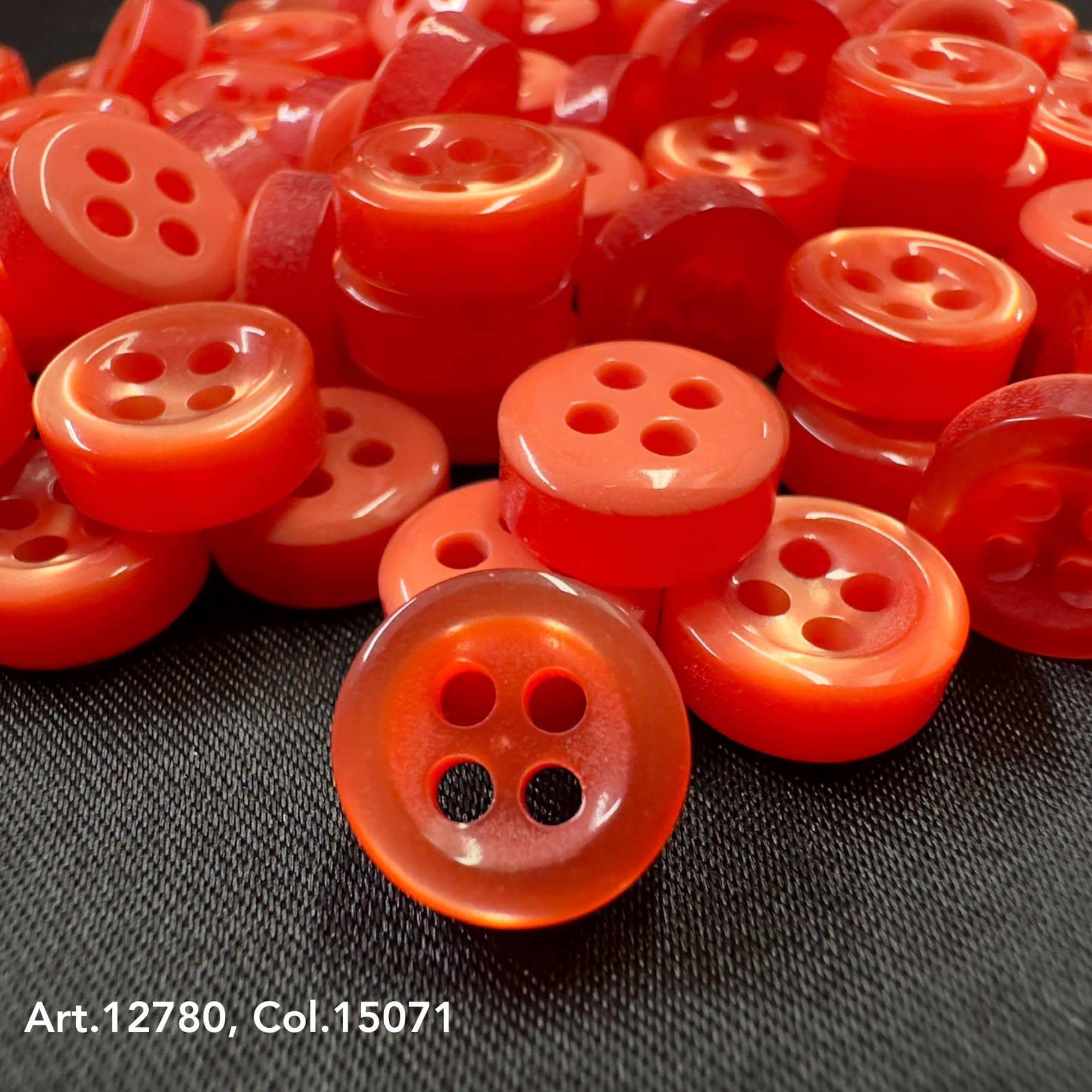 18L four hole plastic buttons in bright red stacked on black fabric by Buttonology Inc