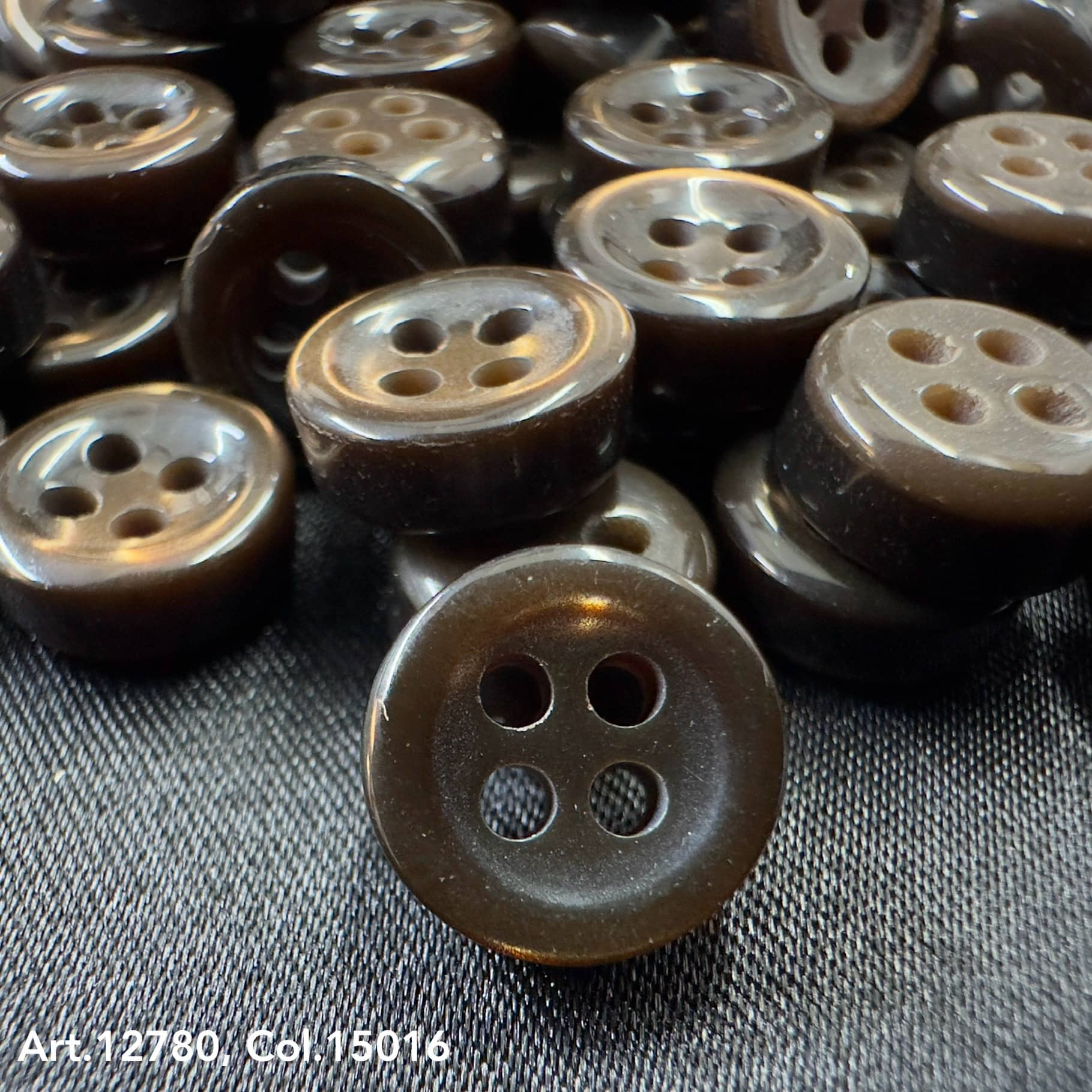Buttonology Inc 18L four hole plastic buttons in dark brown color on fabric background