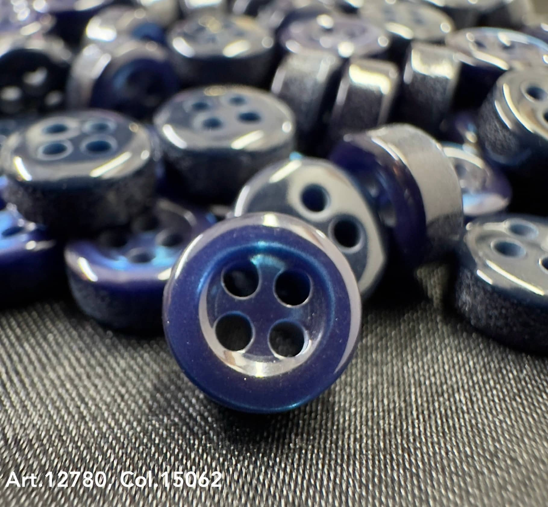 Close-up of 18L four hole plastic buttons in dark blue from Buttonology Inc on fabric surface