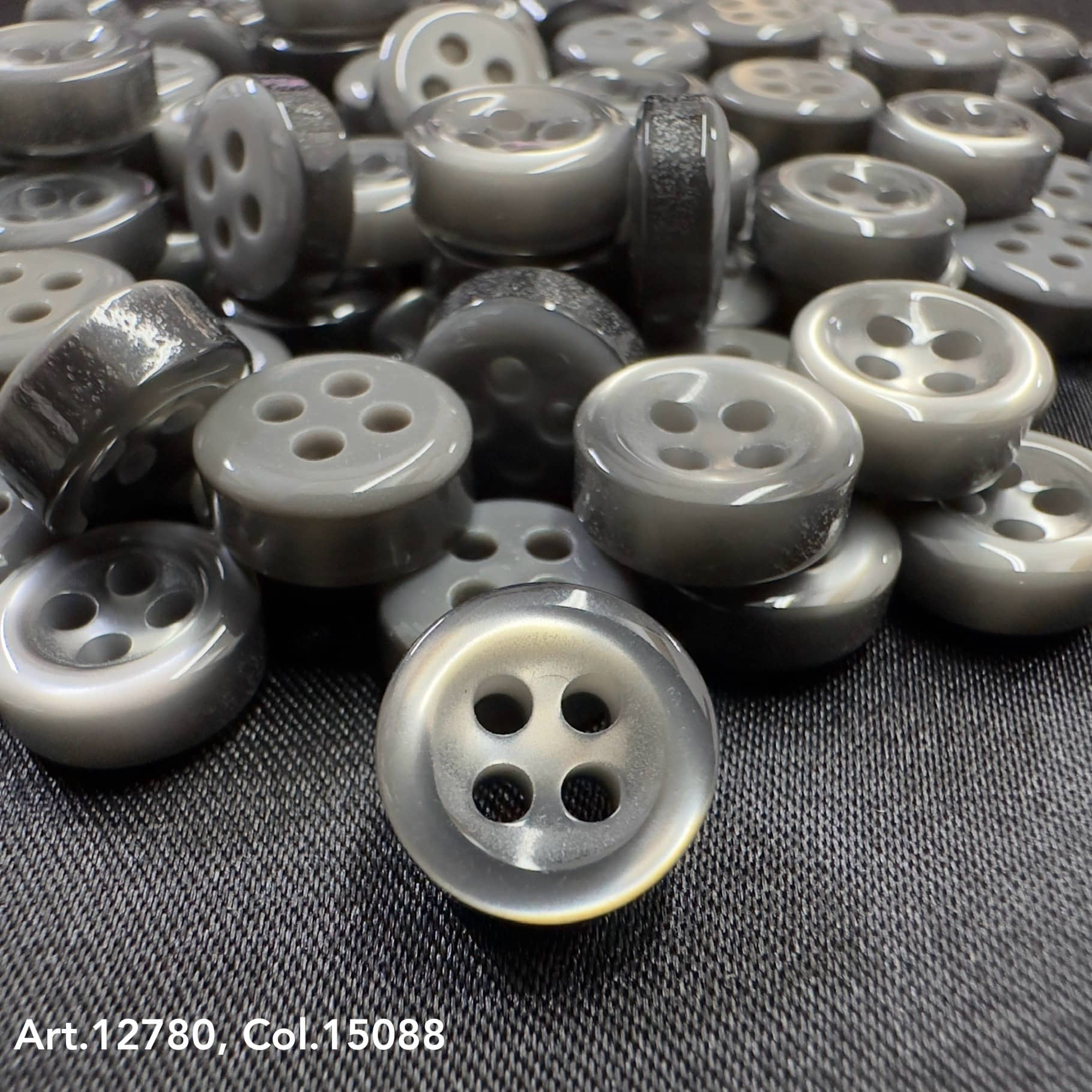 18L four hole plastic buttons in gray shade from Buttonology Inc pile on black fabric