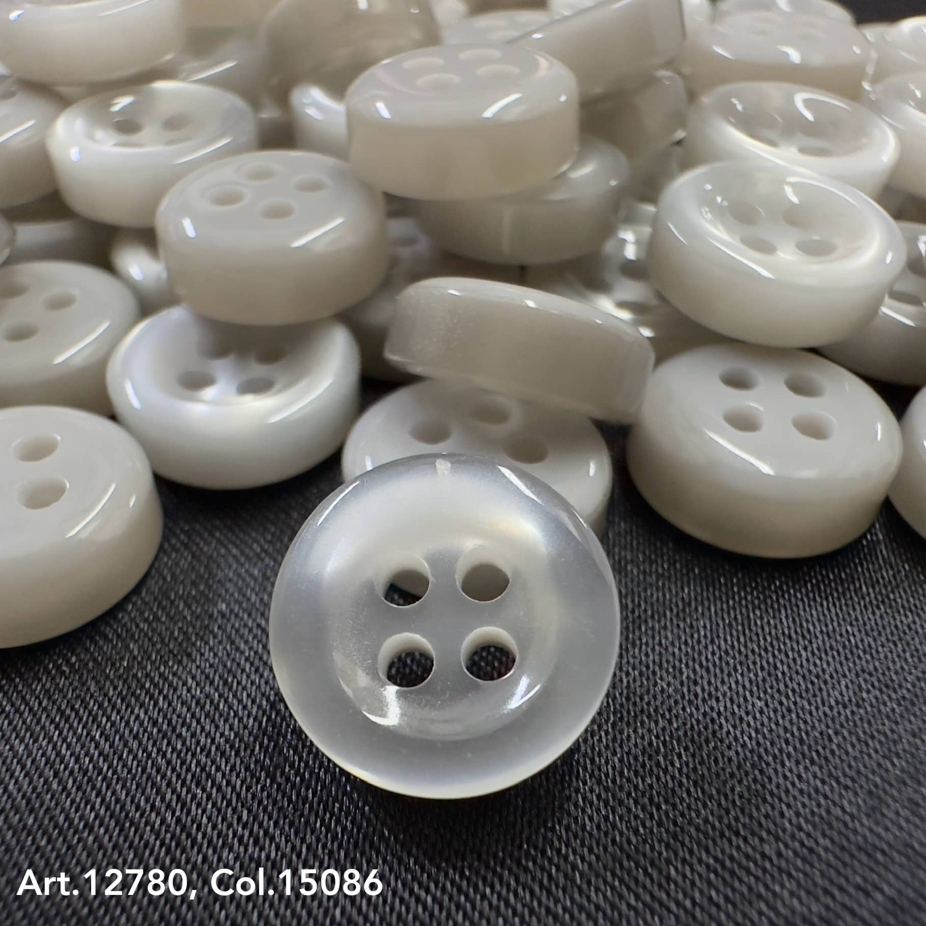 18L four hole plastic buttons by Buttonology Inc in translucent white on black fabric background