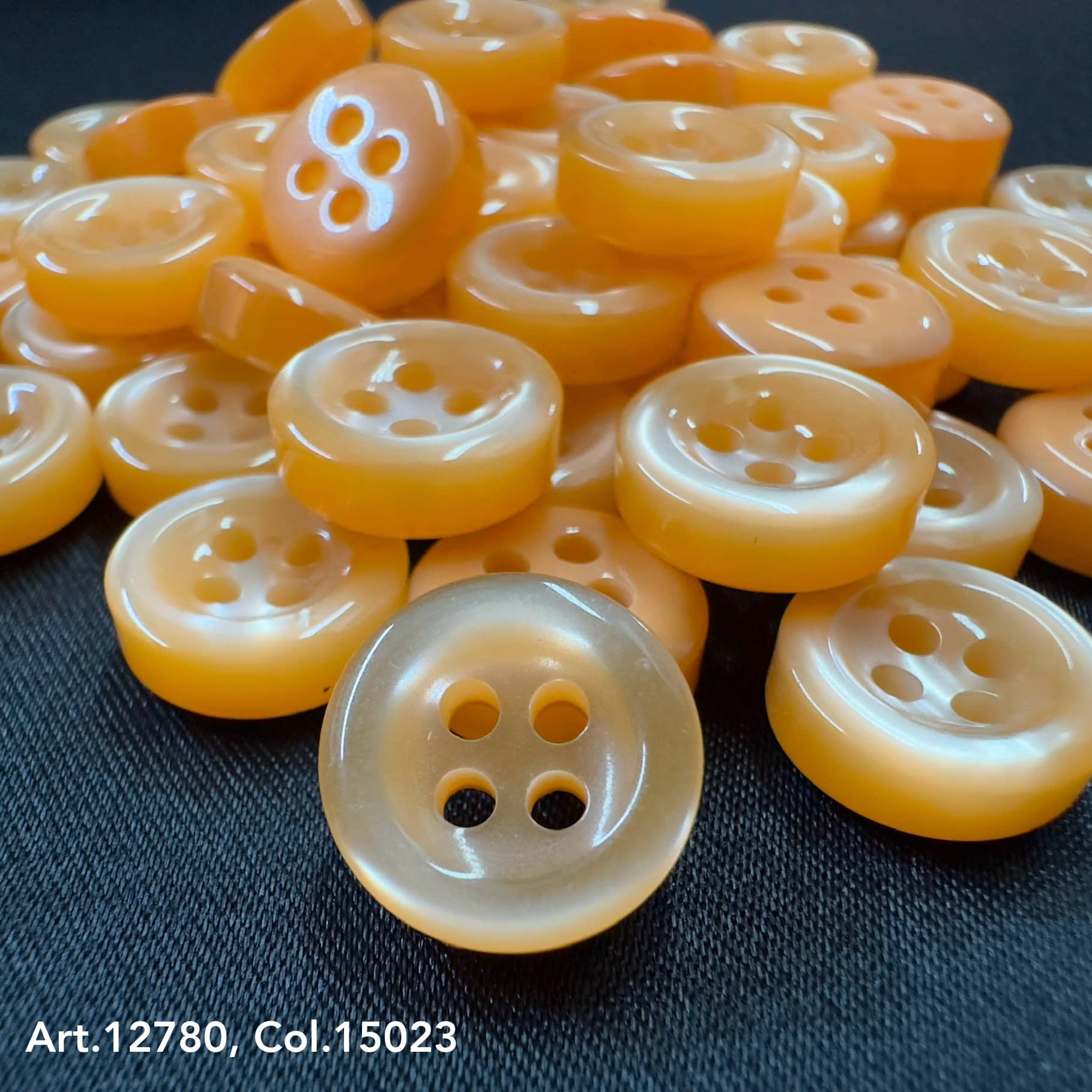 18L four hole plastic buttons in translucent orange by Buttonology Inc neatly arranged on dark fabric