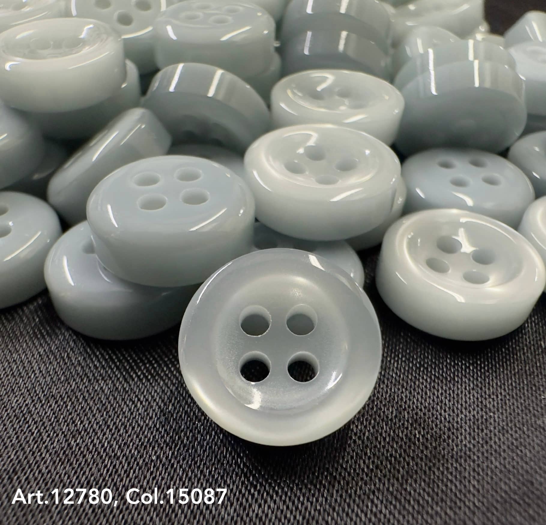 18L four hole plastic buttons in a soft gray color by Buttonology Inc, arranged on fabric