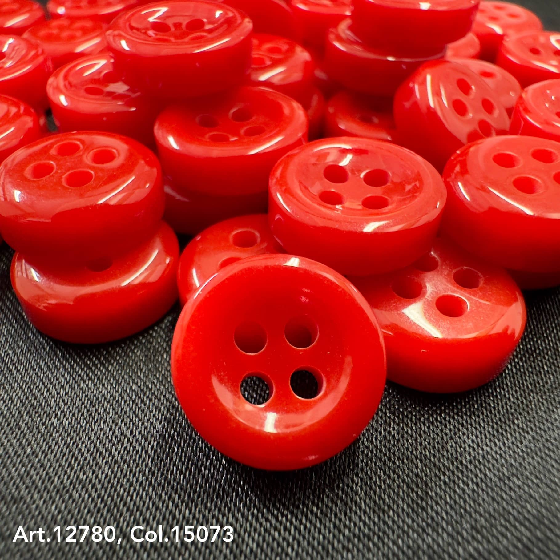 Bright red 18L four hole plastic buttons by Buttonology Inc on black fabric background