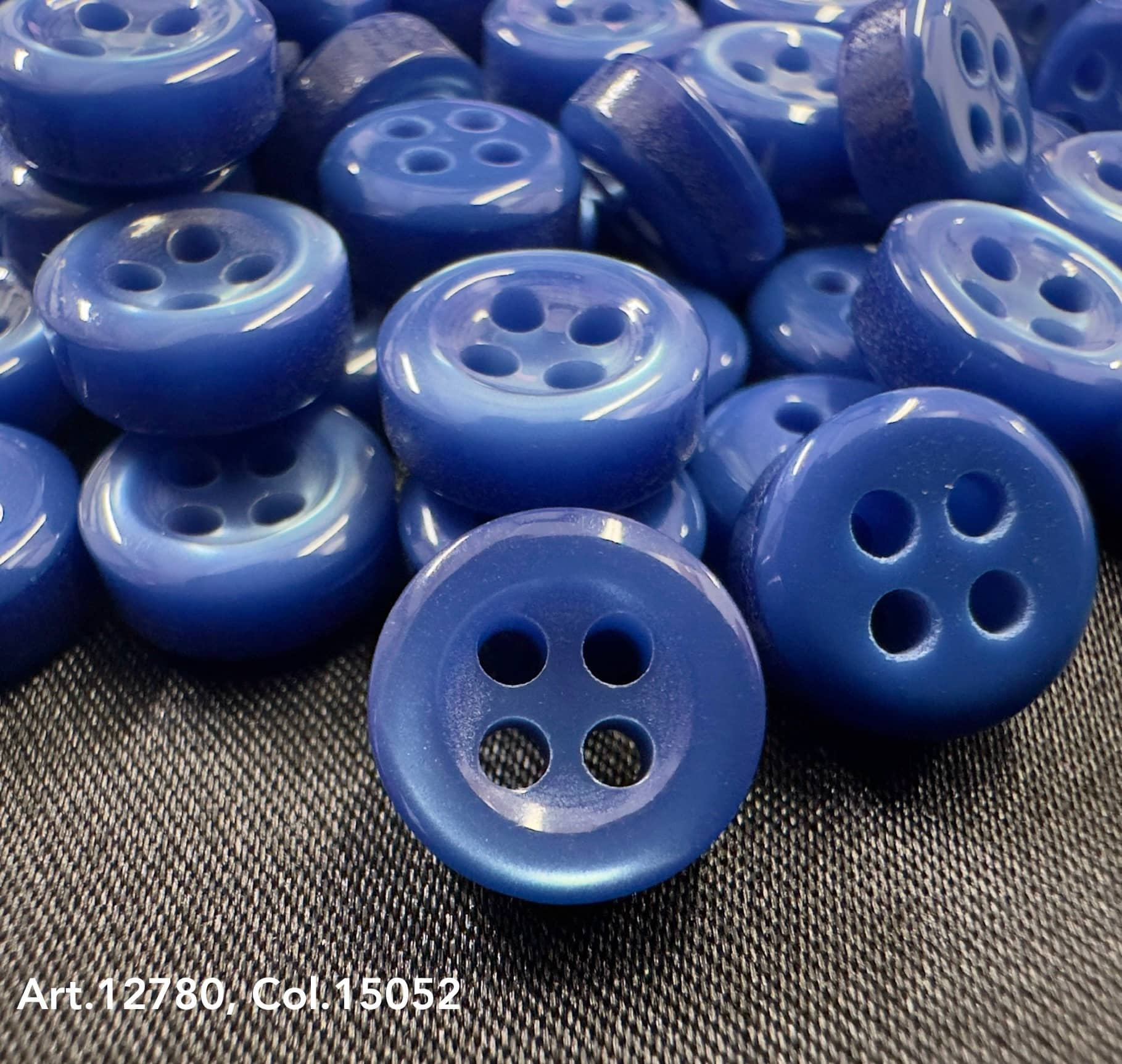Close-up of blue 18L four hole plastic buttons scattered on fabric surface from Buttonology Inc