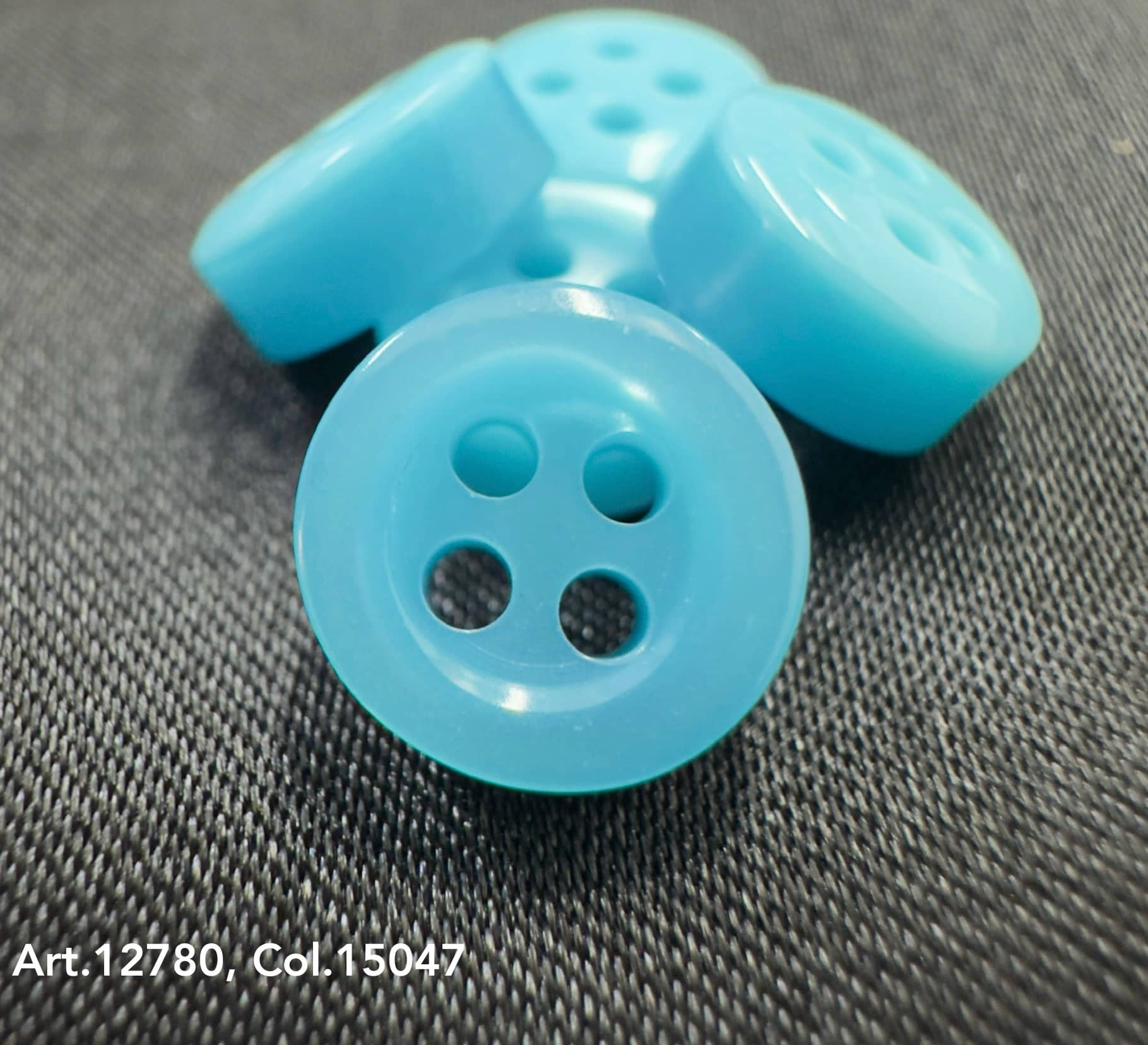 18L four hole plastic buttons in light blue by Buttonology Inc on black fabric background