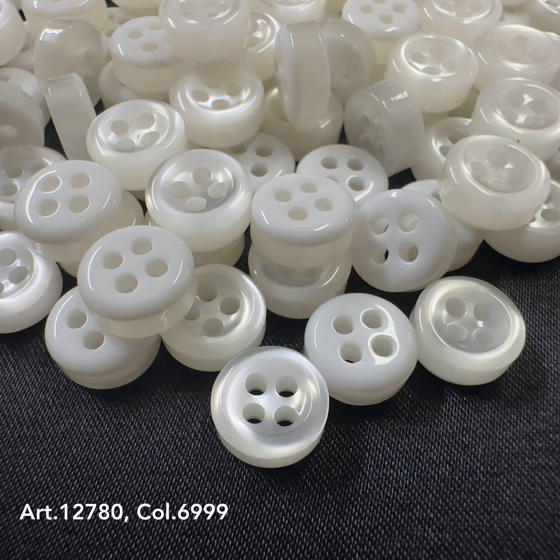 18L four hole plastic buttons in white color from Buttonology Inc scattered on dark fabric